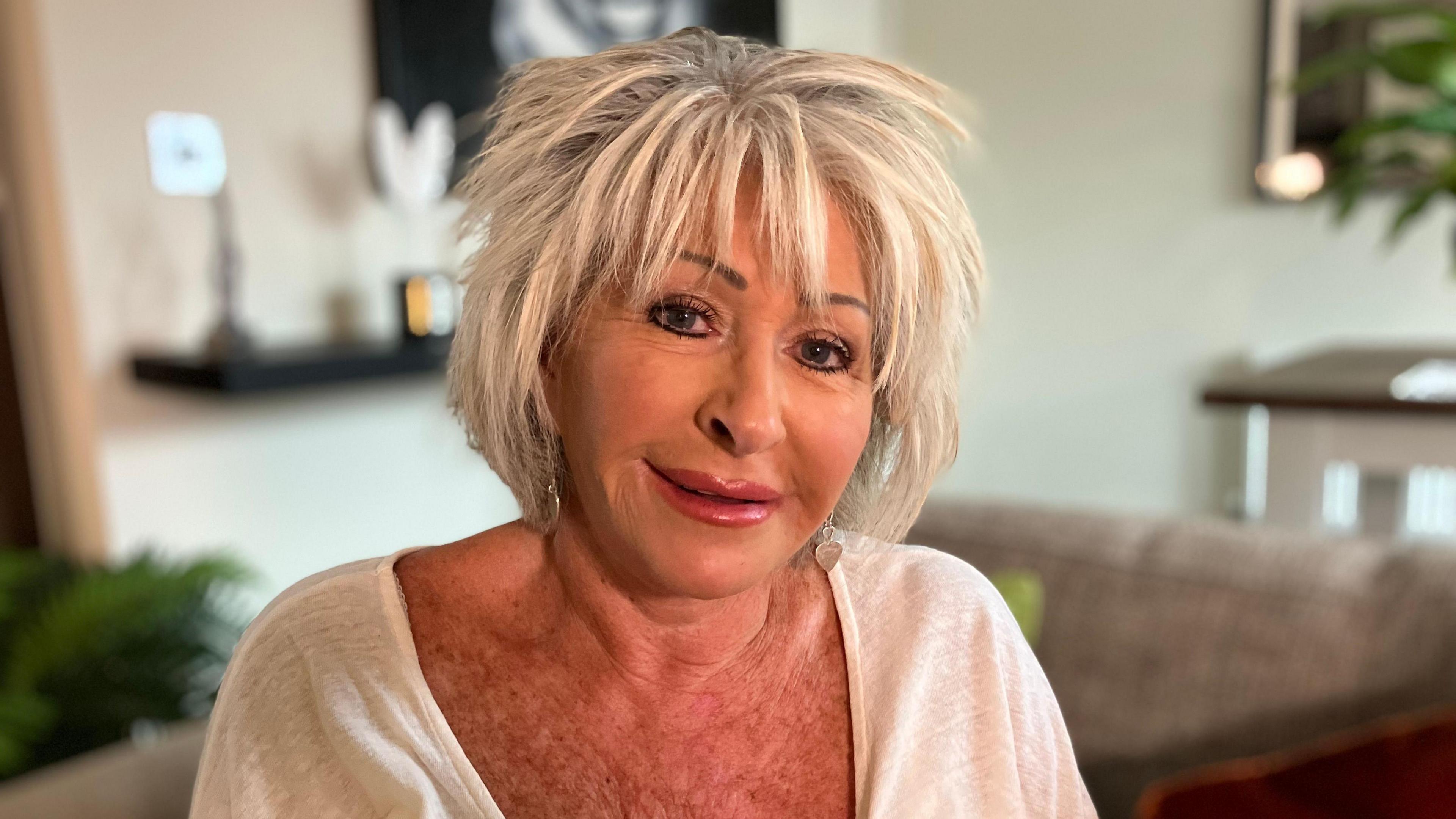 A woman with short blonde hair, smiles at the camera in a living room 