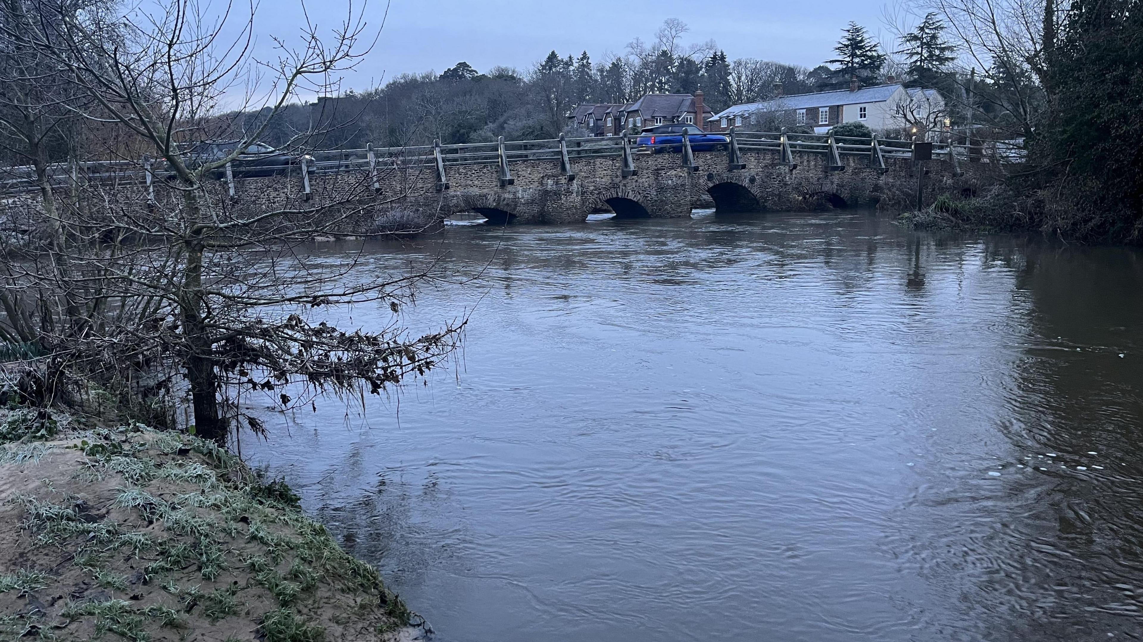 A river which has a high water level with a brick bridge in the background.