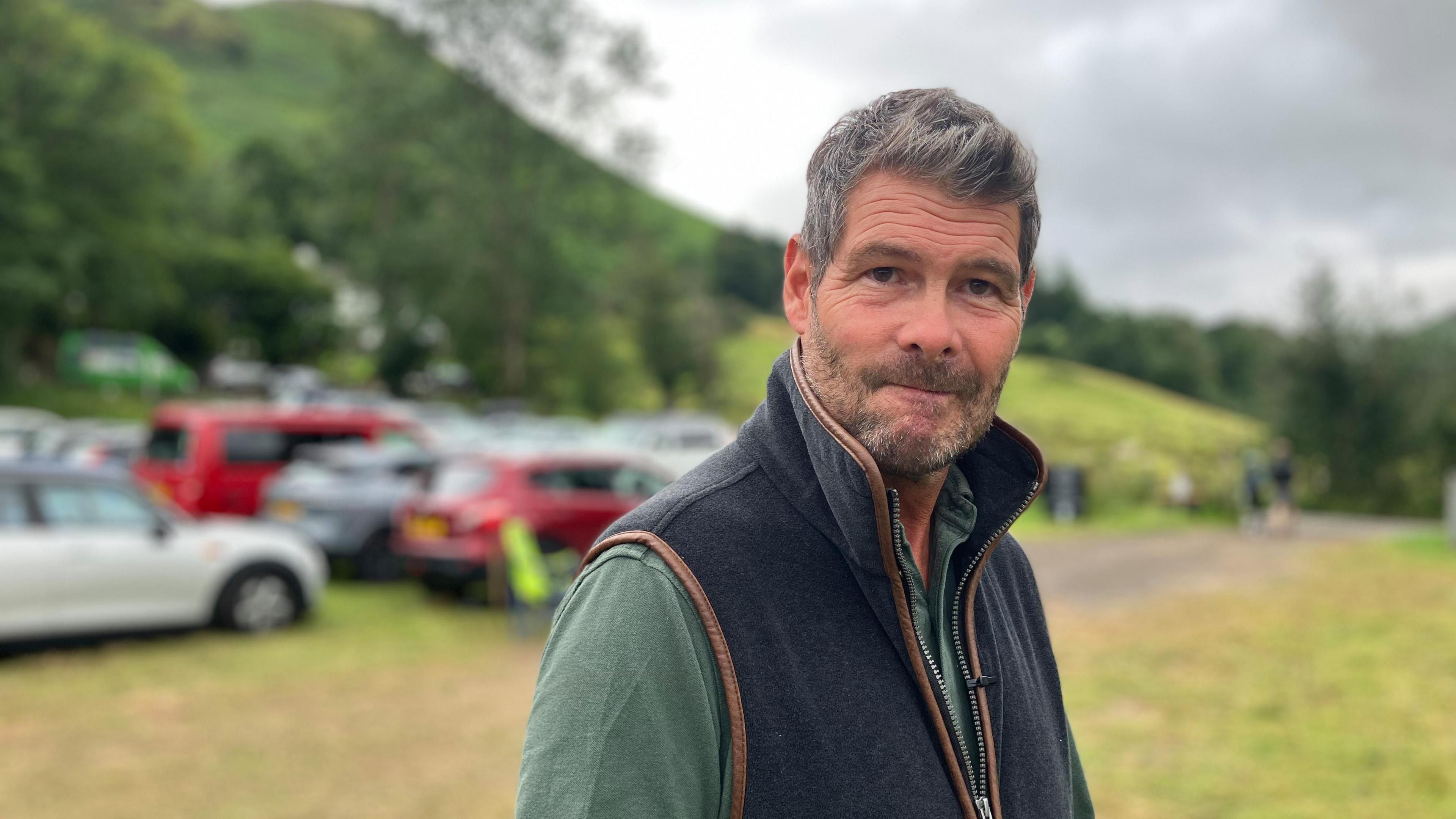 Mike Anderton is standing in a Lake District field, which is being used as a car park.