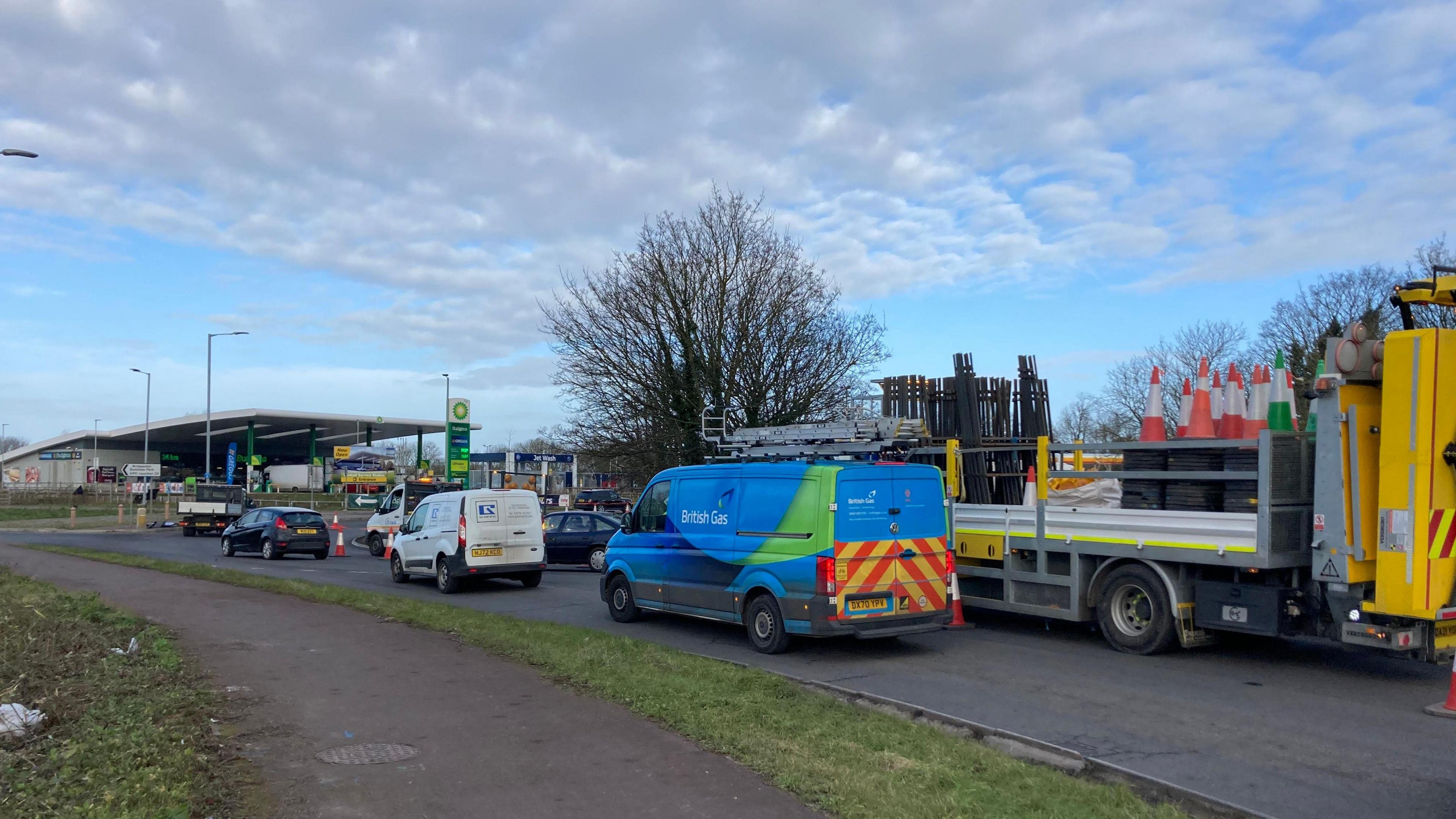 Traffic queuing and big yellow lorry with traffic cones with a BP green petrol garage in the background.