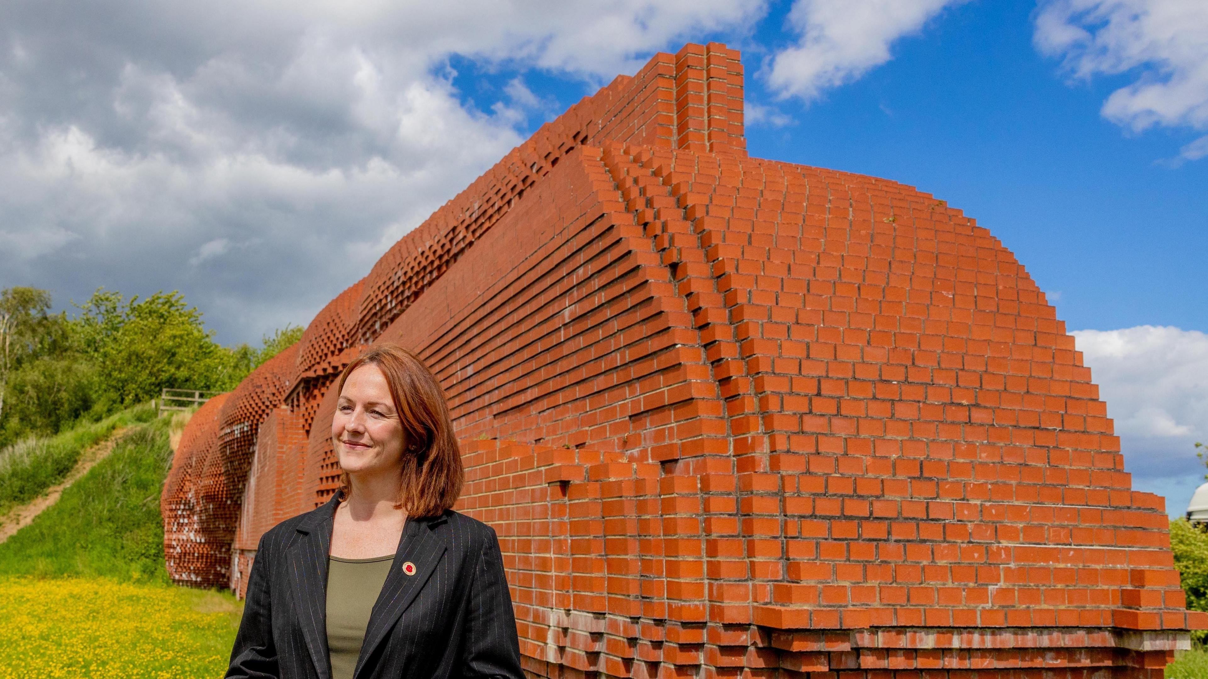 Lola McEvoy, Darlington MP, stands smiling next to the Darlington brick train. She is wearing a green top and a black suit jacket.
