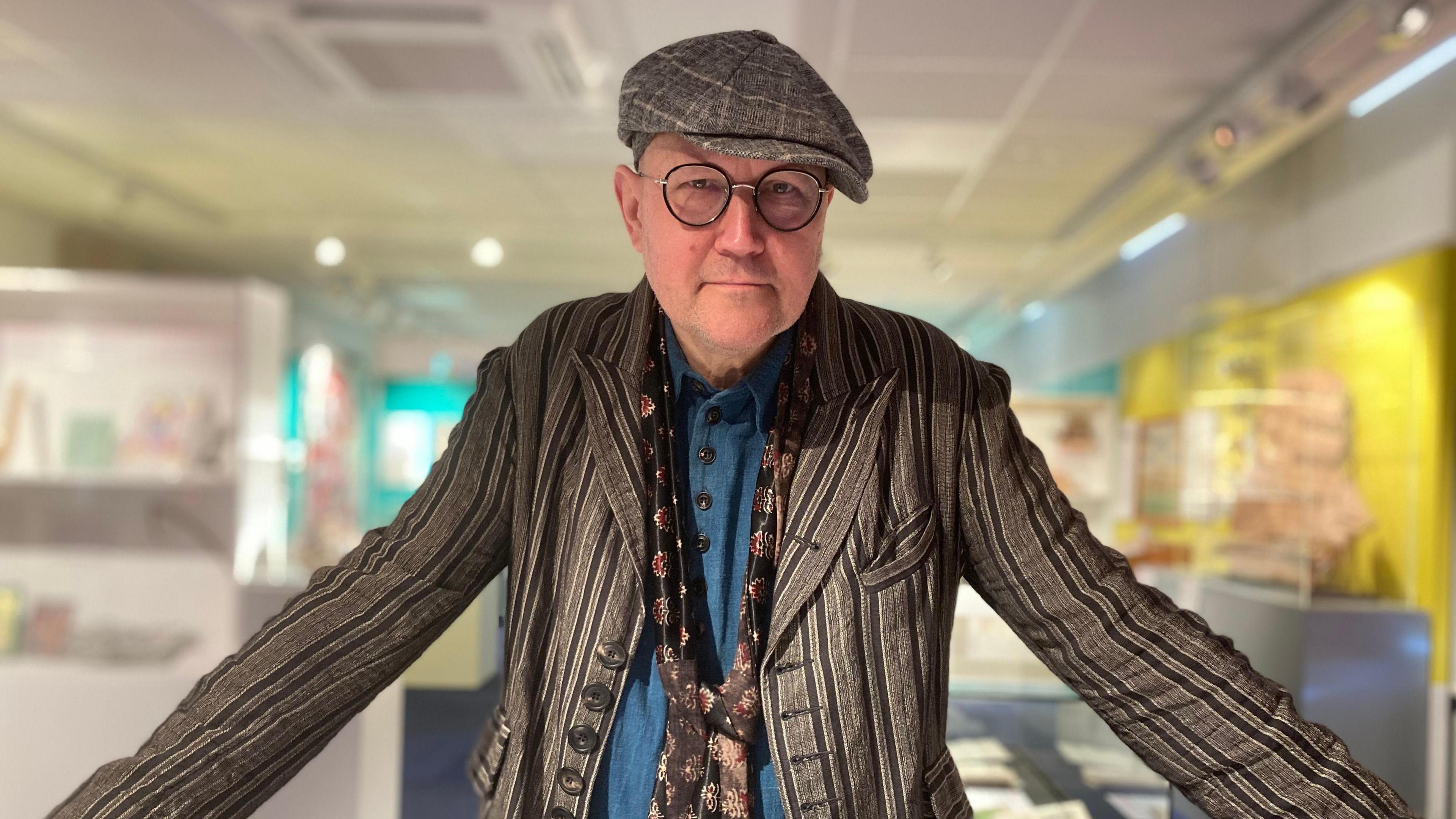 Simon Costin - from the Museum of British Folklore - leaning over a display case, wearing a flatcap and striped jacket