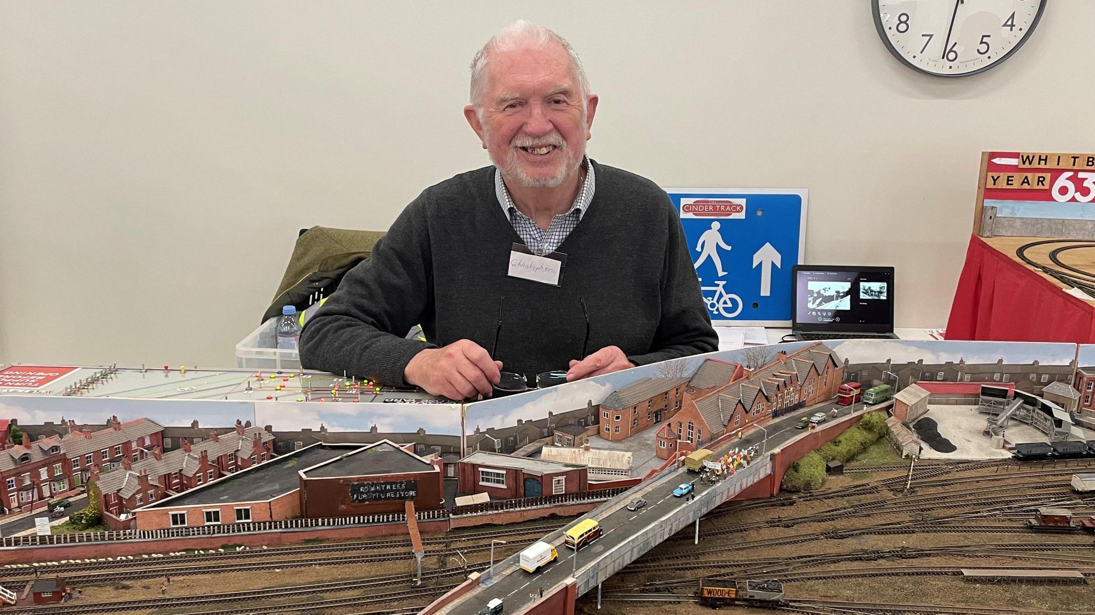 Chris Martin with his model railway, based on part of the Scarborough to Whitby line. Mr Martin, who has short grey hair and a grey goatee, is smiling in the photo.