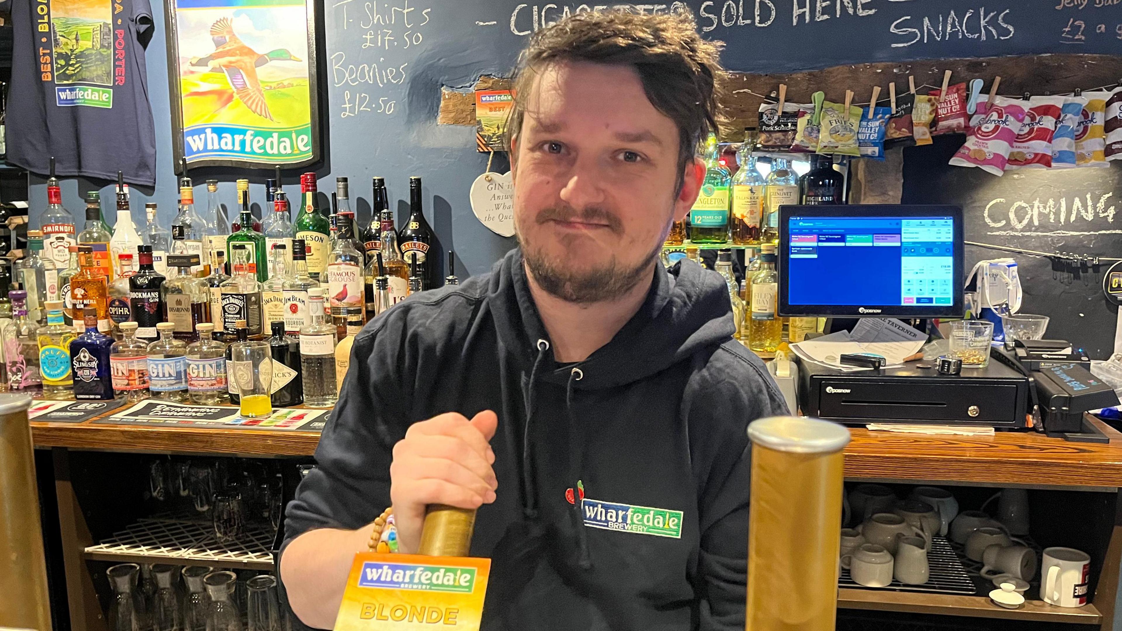 Kyle Hamilton wears an blue hooded top as he stands behind the bar pulling a pint.