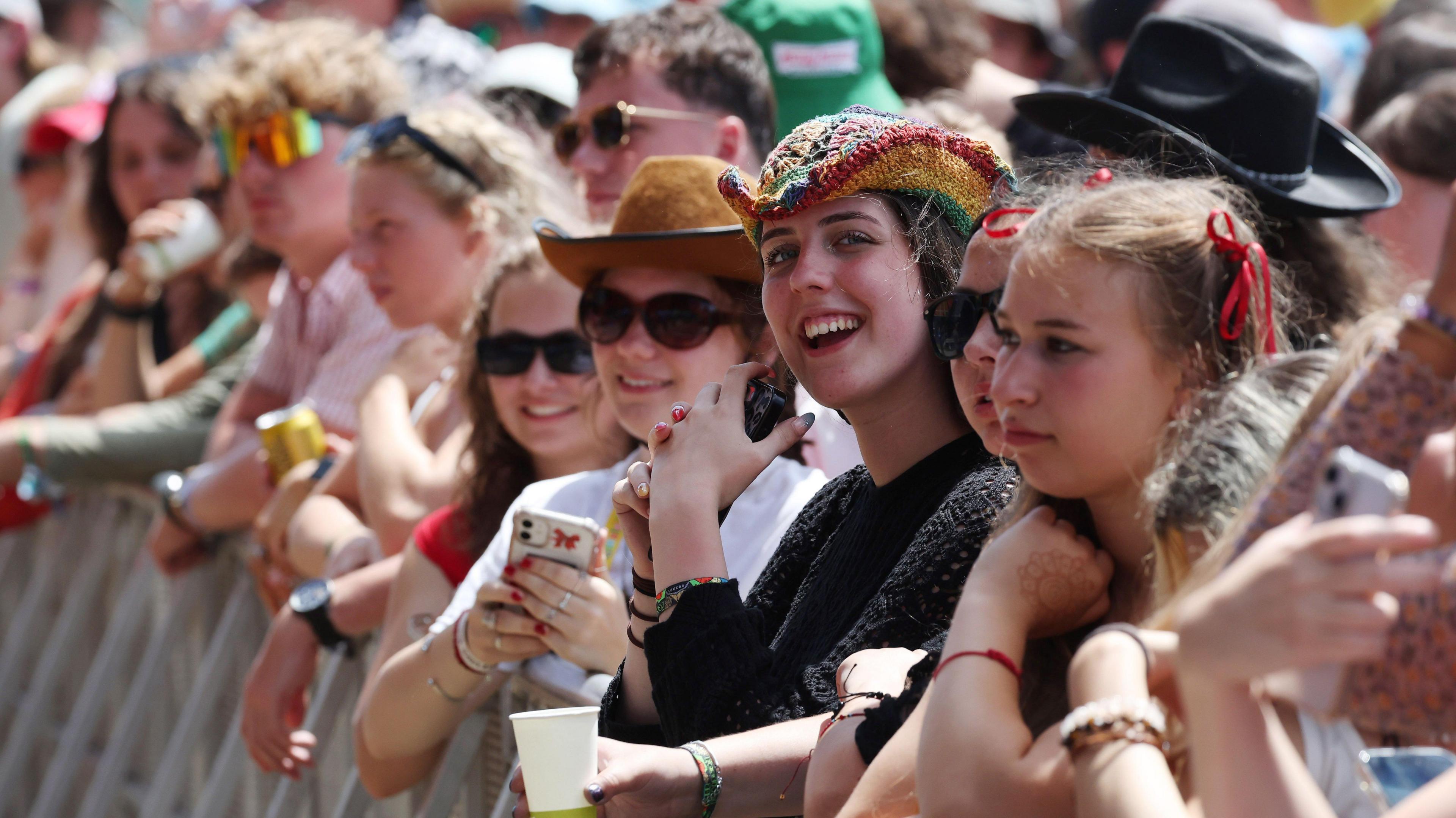 A row of women in the front of a crowd looking at Glastonbury's main stage. Some of them are wearing hats and sunglasses.