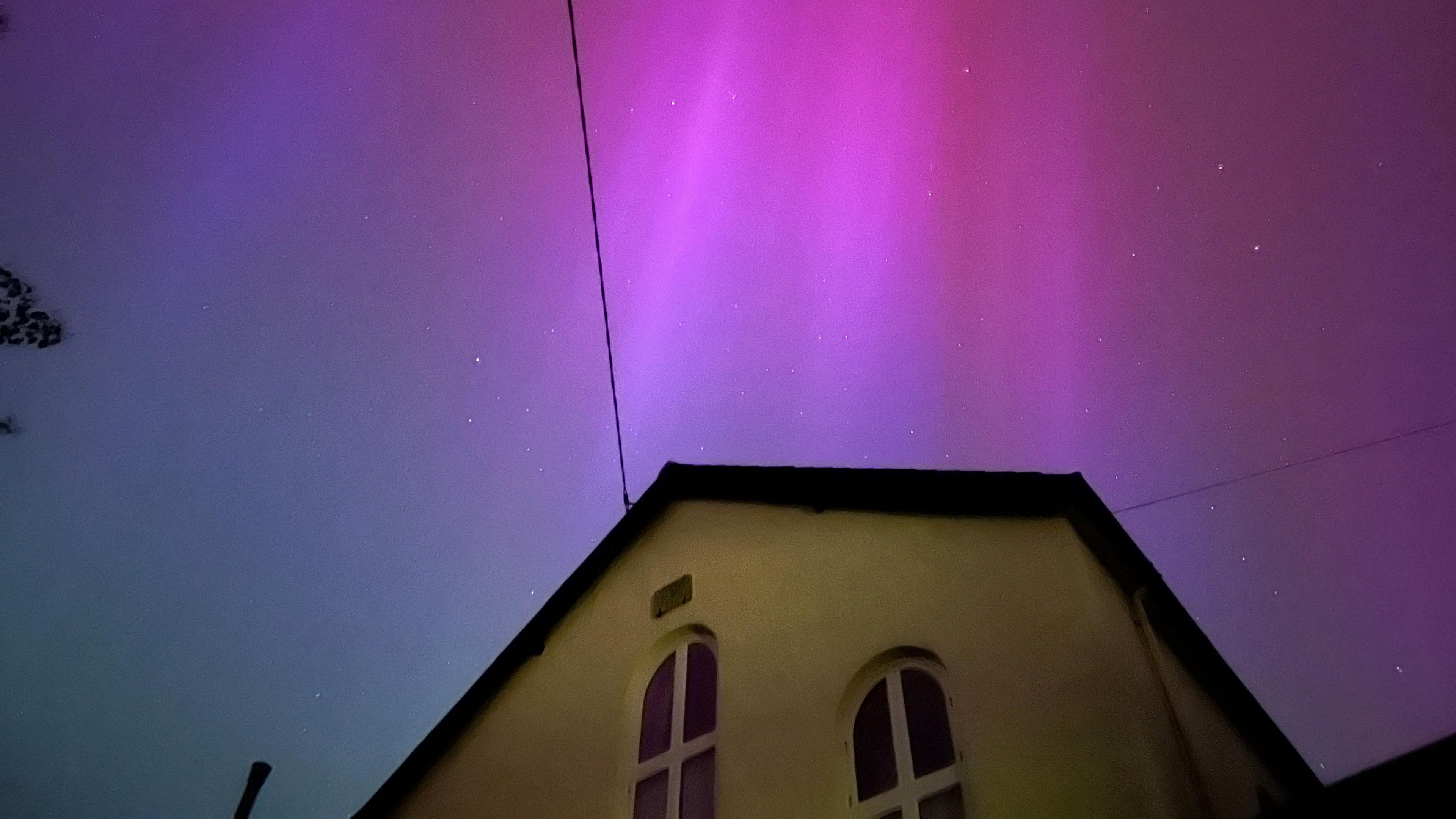 Aurora borealis over a building in Christow in Devon. It has a pink and purple colour in the sky above the yellow building.