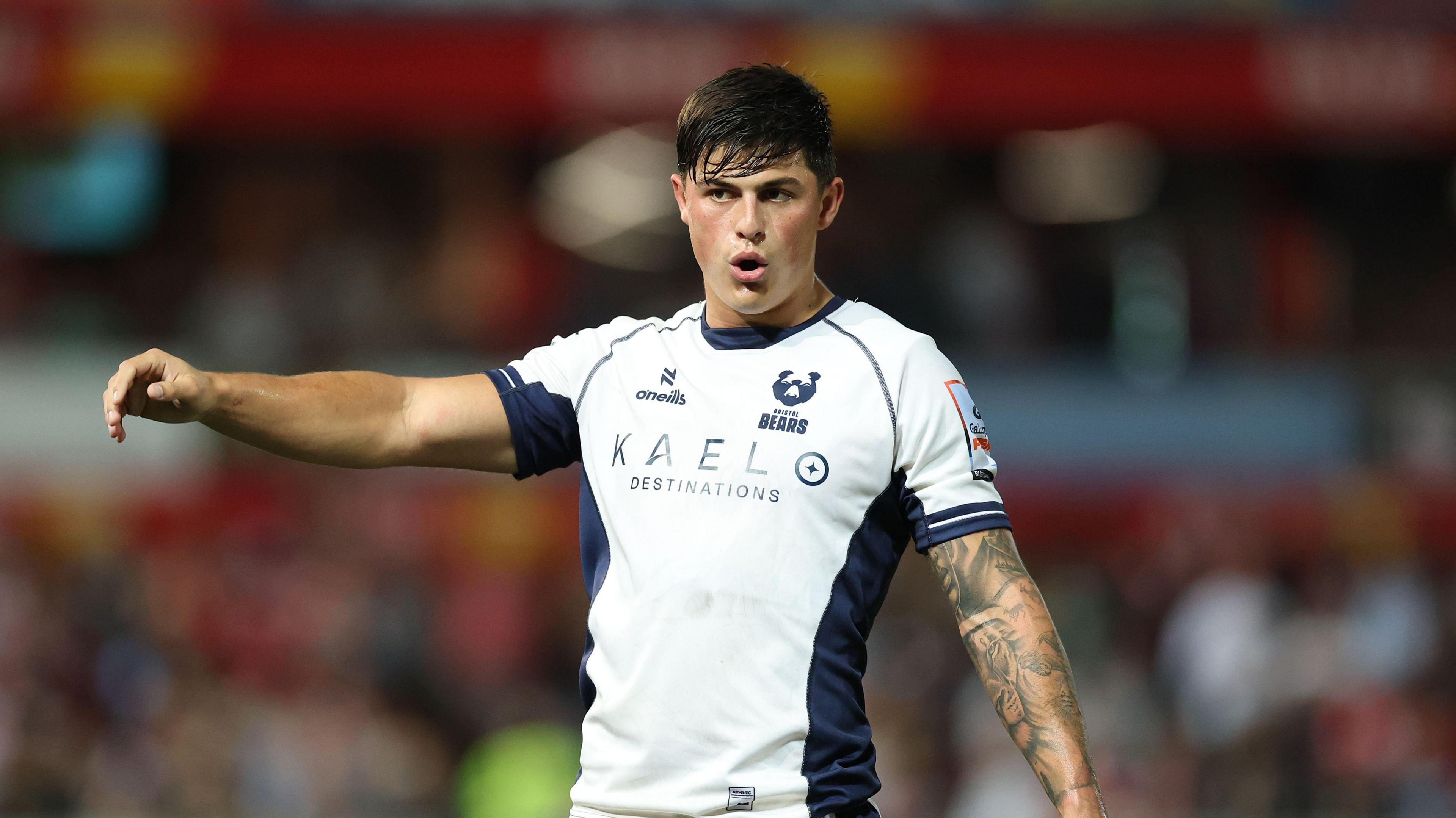 A rugby player looking away from the camera with his arm in the air. 