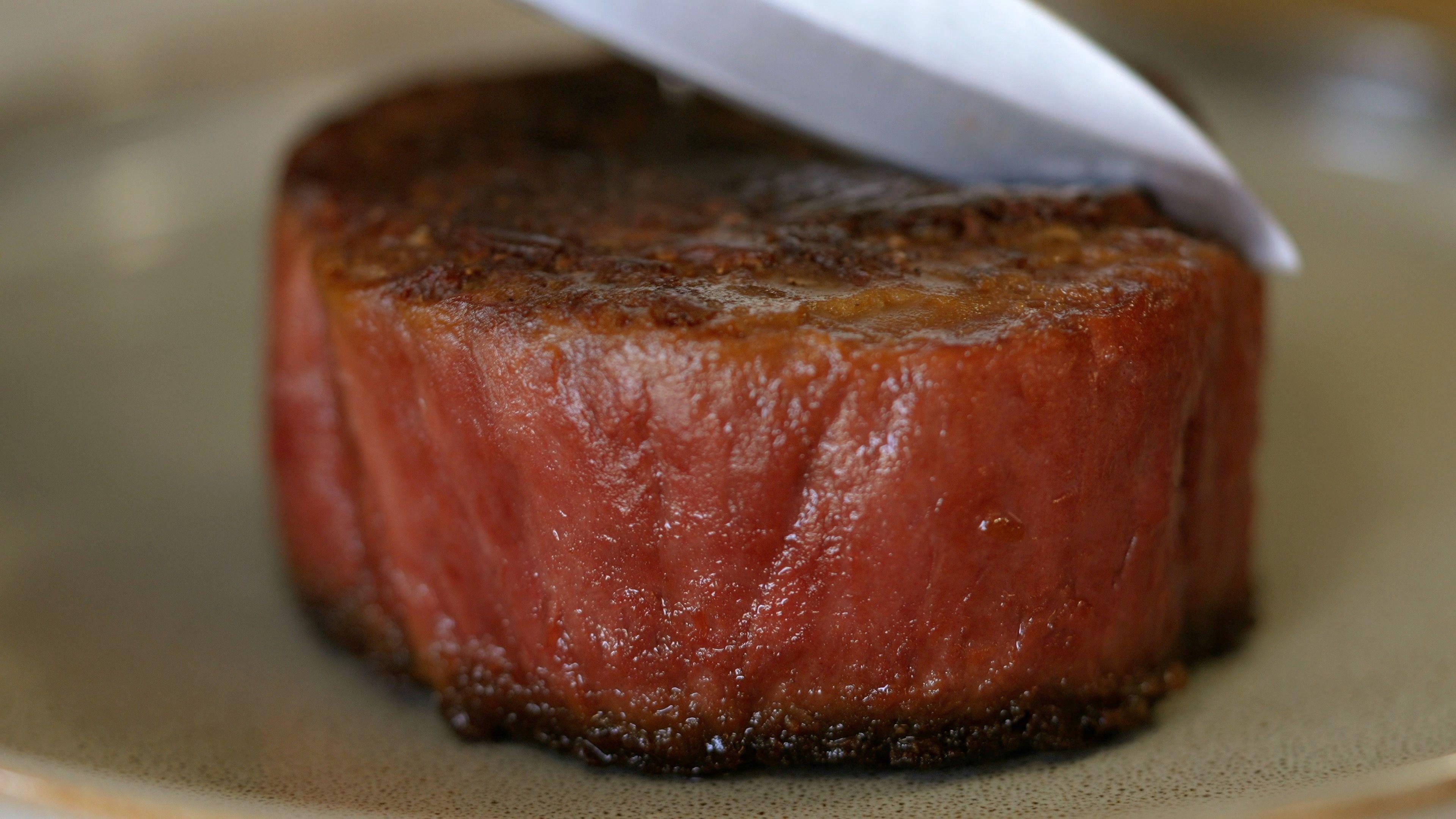 A sirloin steak, well cooked. Dark on the top and pink around the sides. A knife begins to cut it



