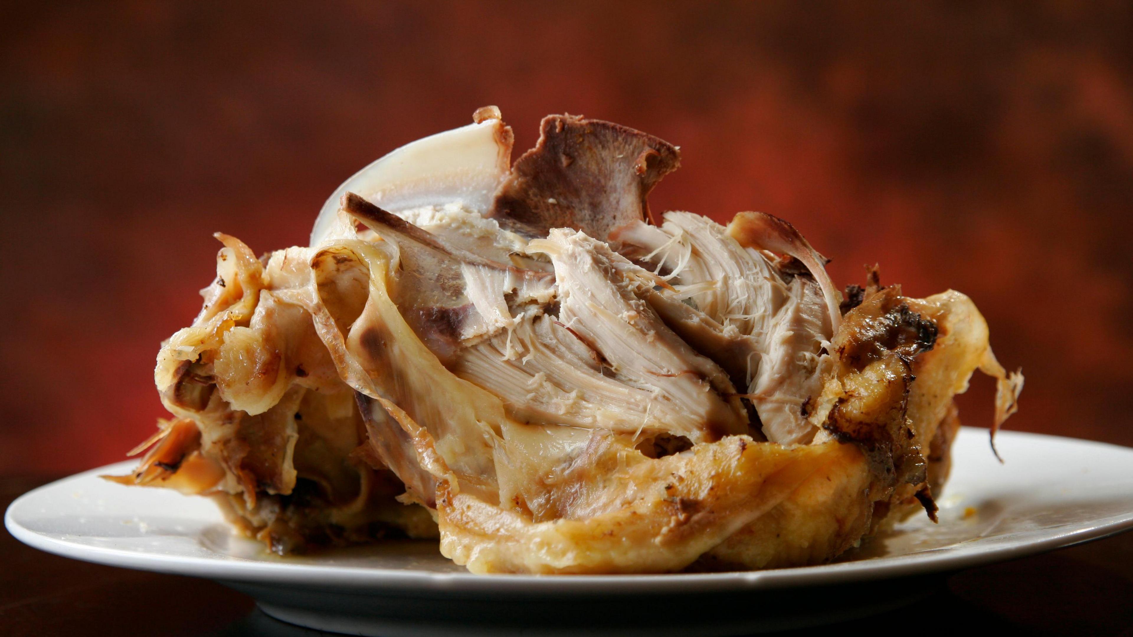 A cooked chicken breast sits on a white plate with a mottled red and orange background. It has been half eaten so you can start to see the bones poking through the meat