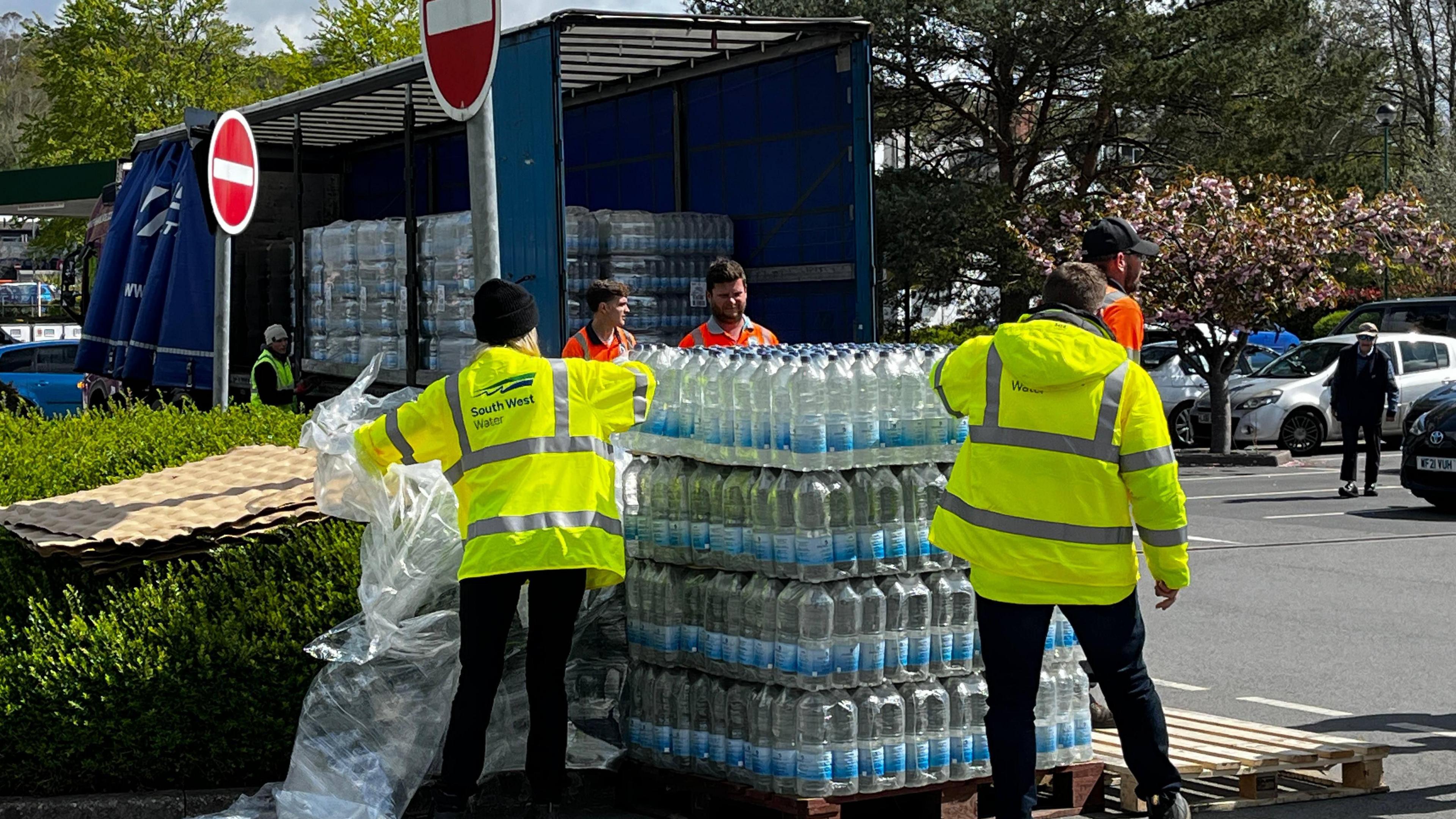 Two people wearing hi-vis moving crates of bottled water from a lorry.