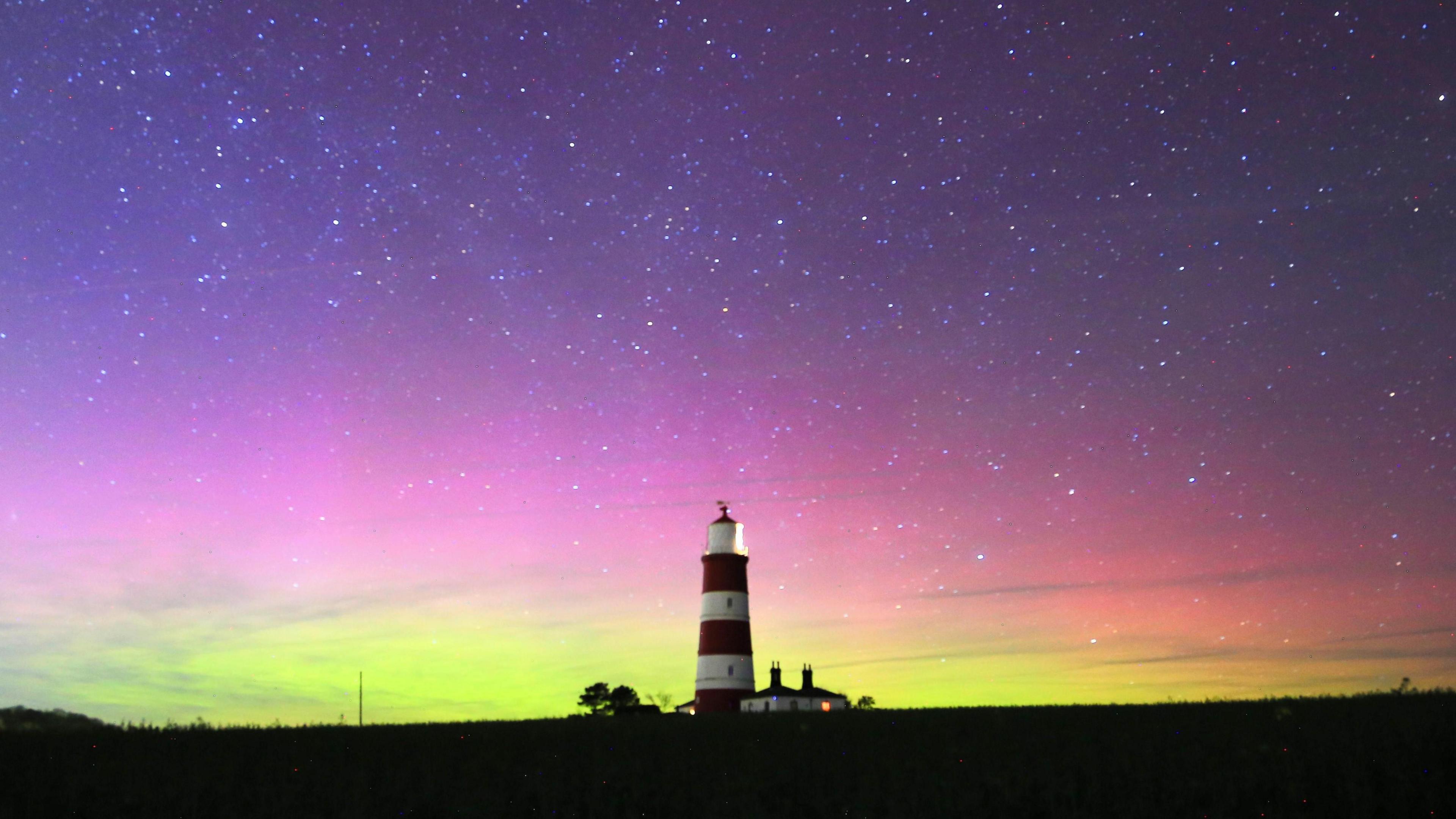 picture of a lighthouse with the night sky filled with greens, purples and reds of the northern lights.