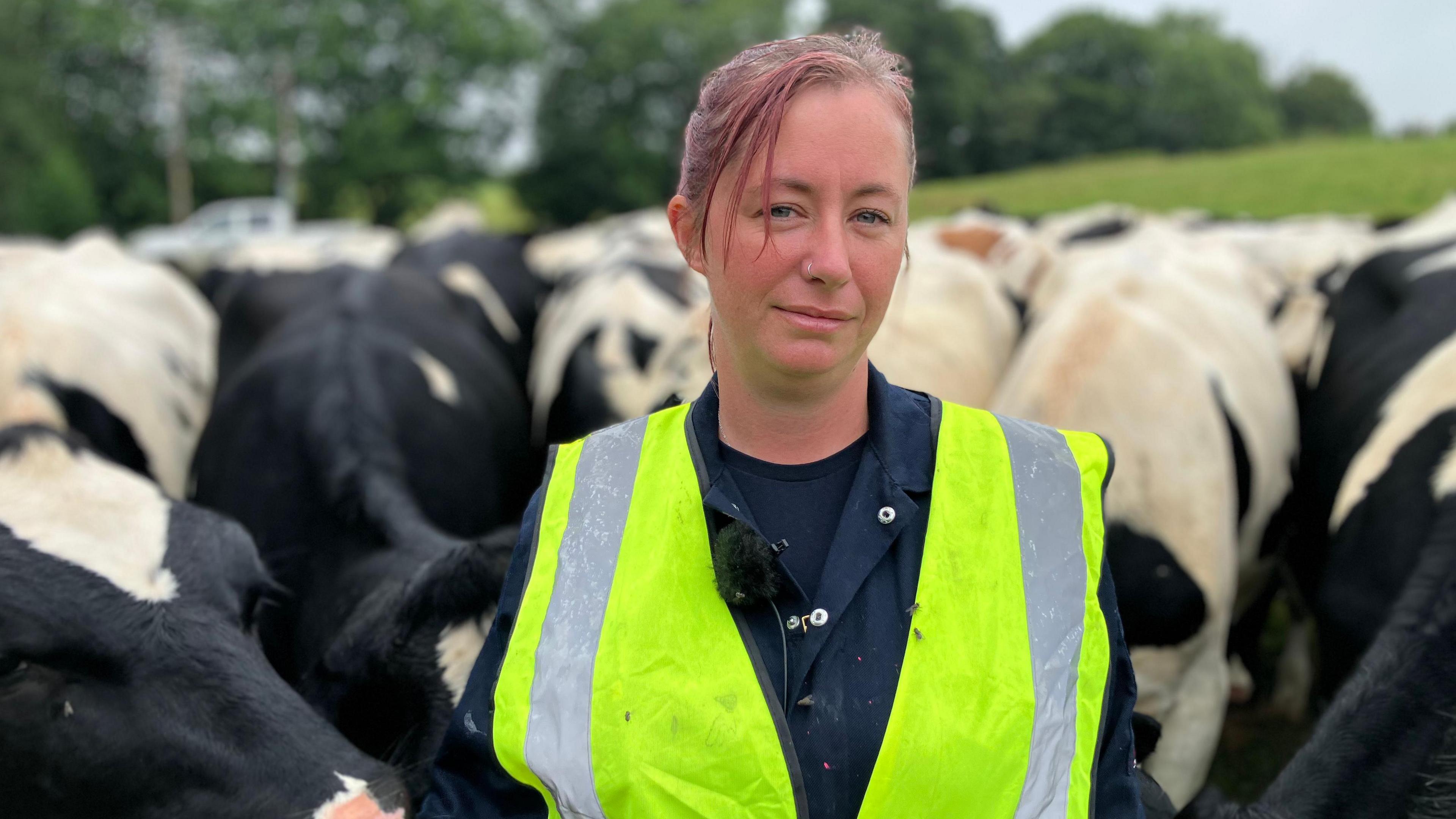 Terri Taylor wearing a high viz vest over her farming overalls is surrounded by black and white cows