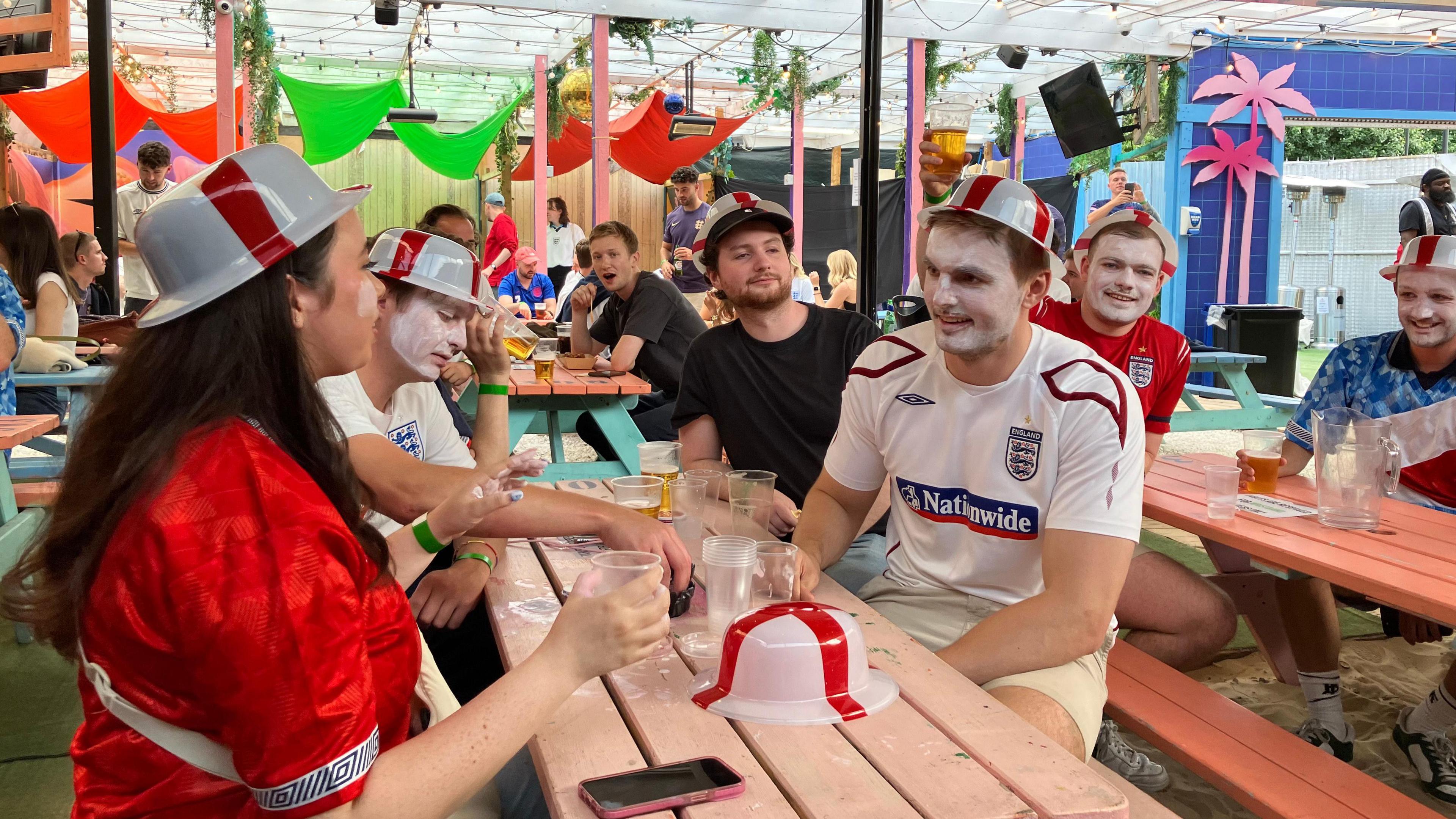 People sitting in pub beer garden, some with faces painted in England colours