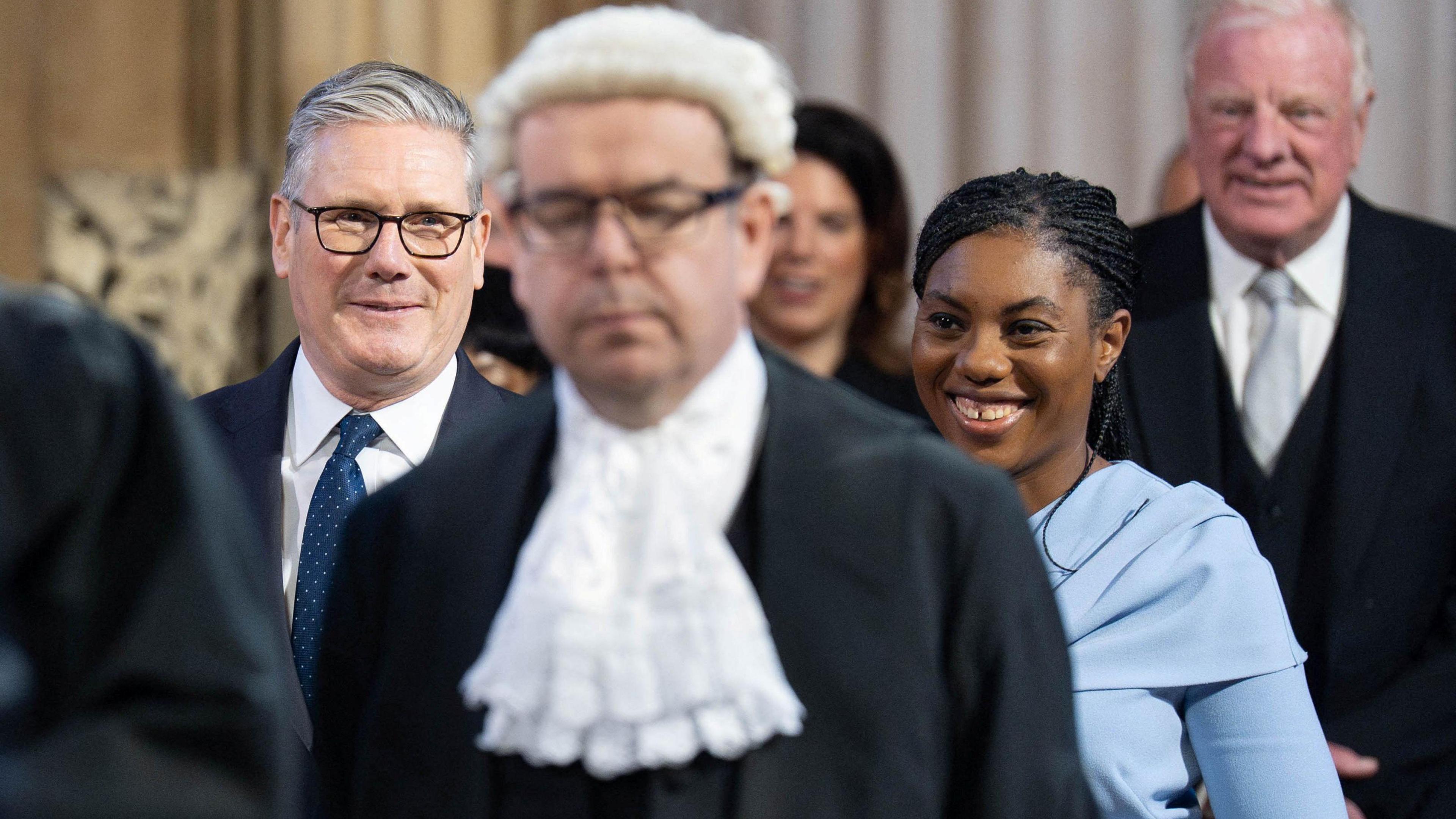 Keir Starmer and kemi badenoch smiling and walking with other people to the king's speech