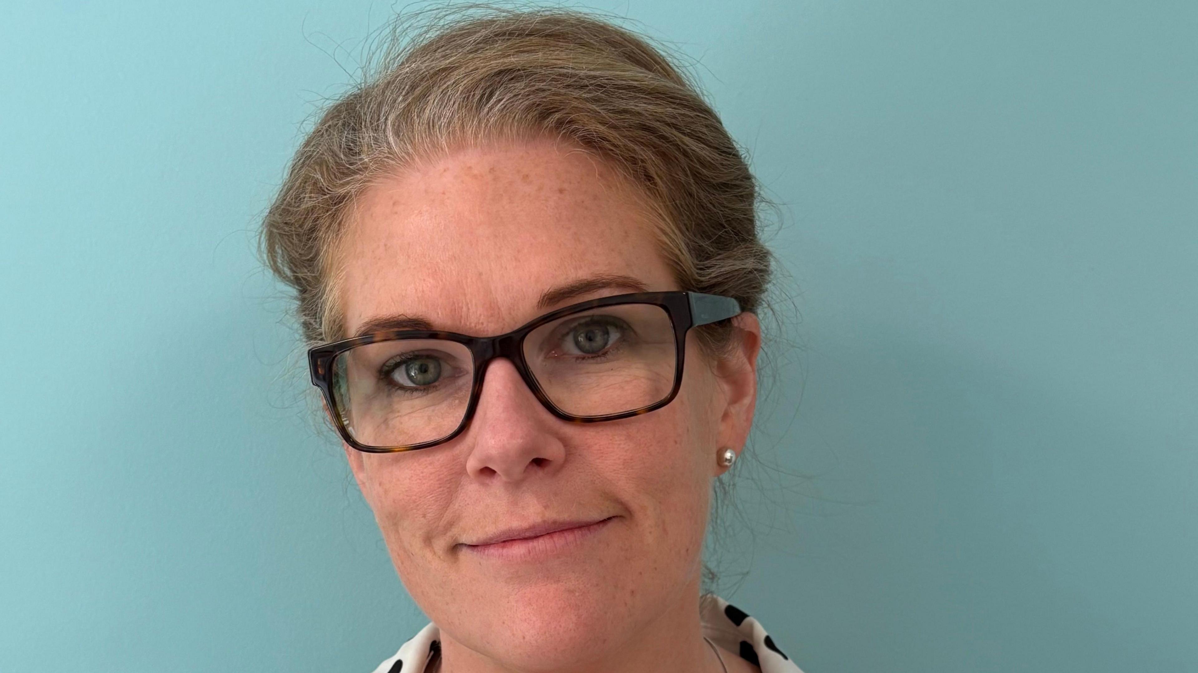 Dr Rebecca Towner with brown hair which is tied back, glasses and pearl earrings smiling at the camera