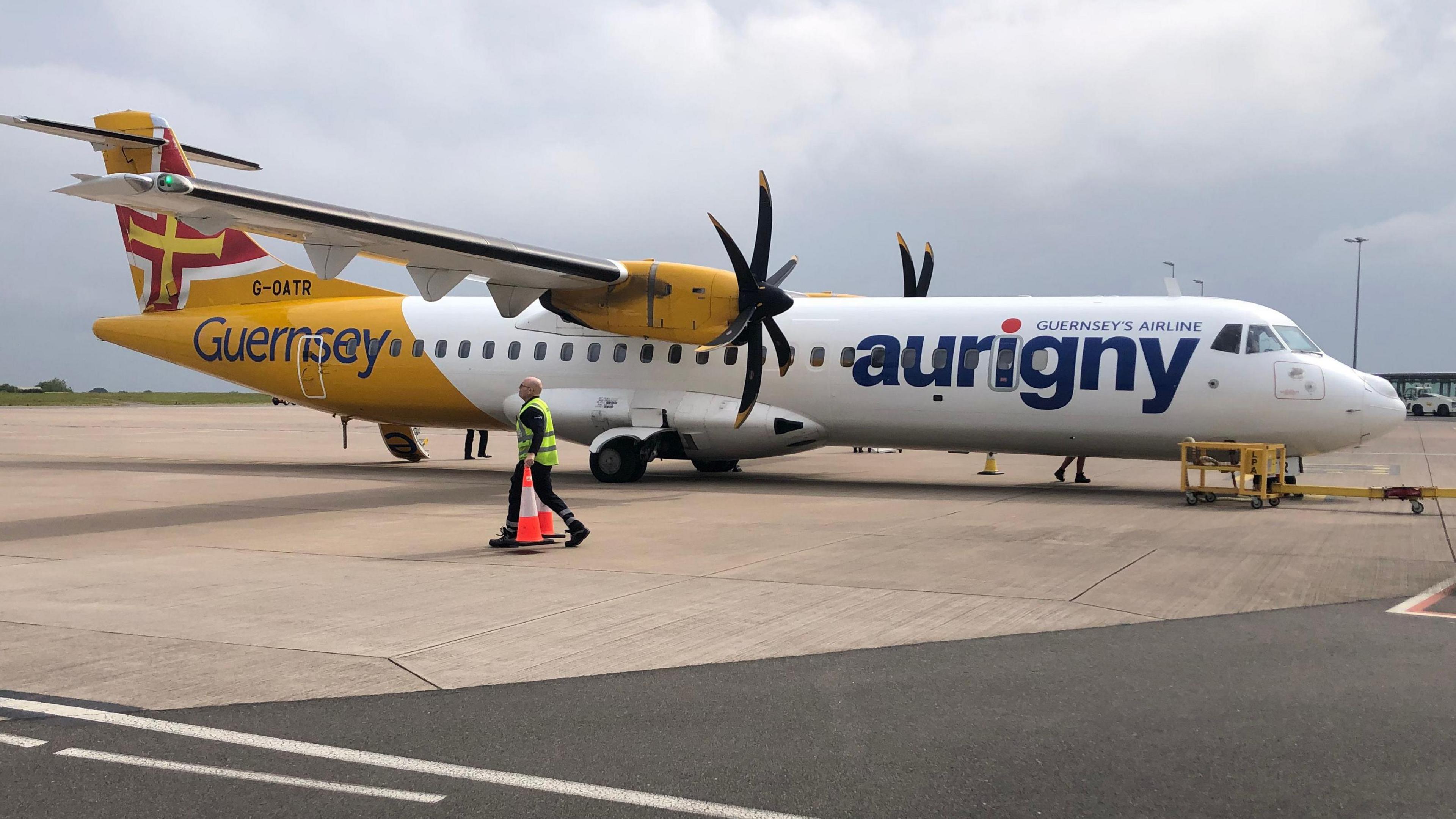 A white and yellow plane with the word Aurigny on the side. Propellors on each wing. 