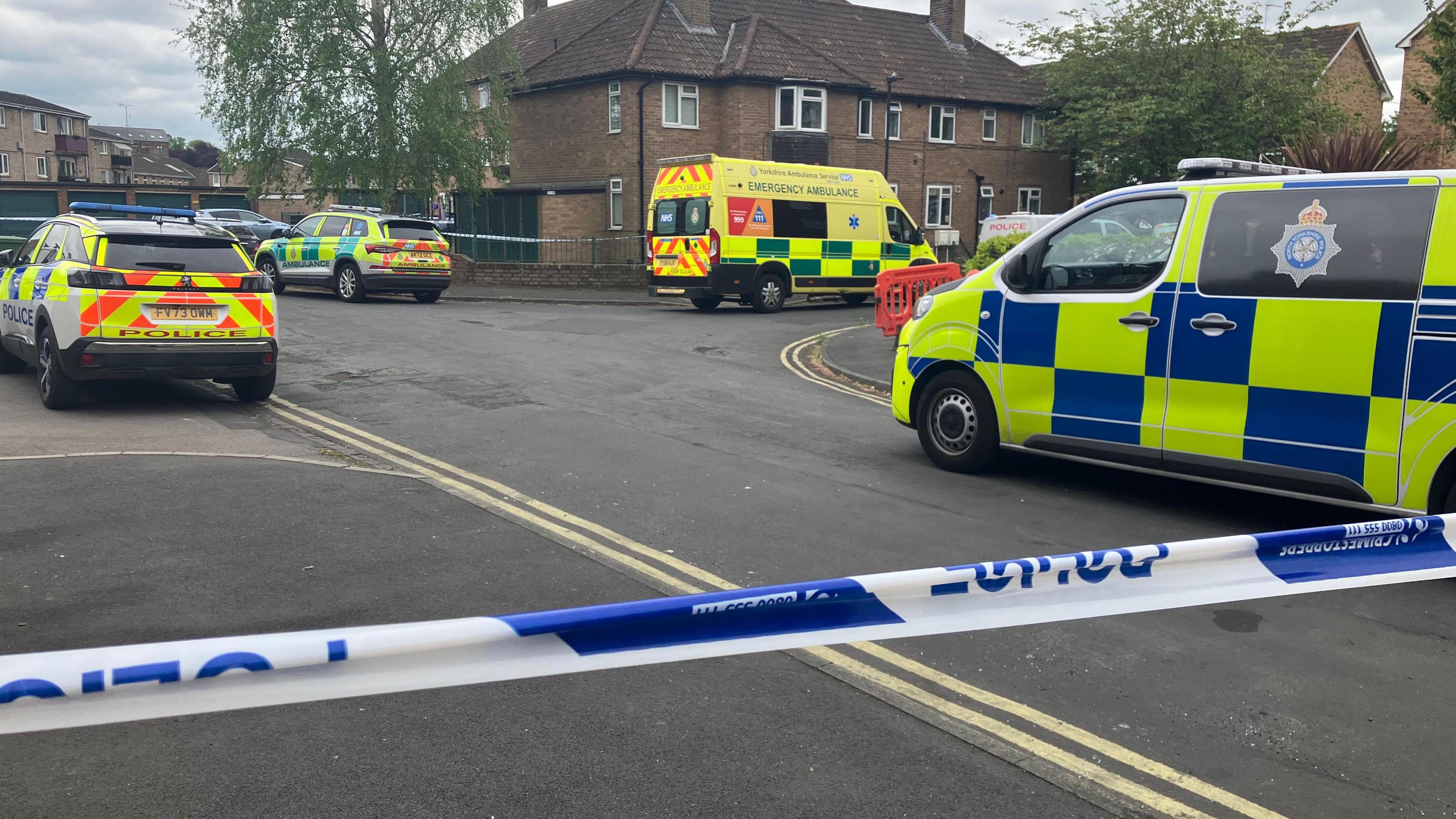 Police vans, cars and ambulances in a cordoned off residential street.