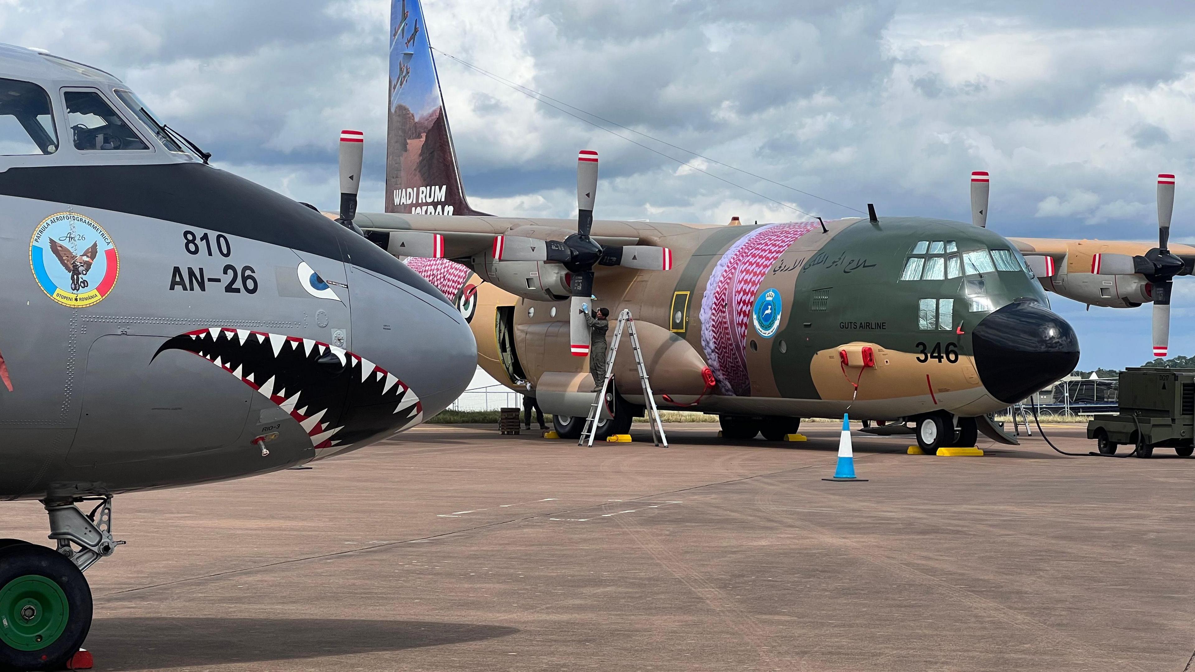 Two colourful aircraft, one with a nose painted like a shark's face, another painted in green and beige with a red scarf around it