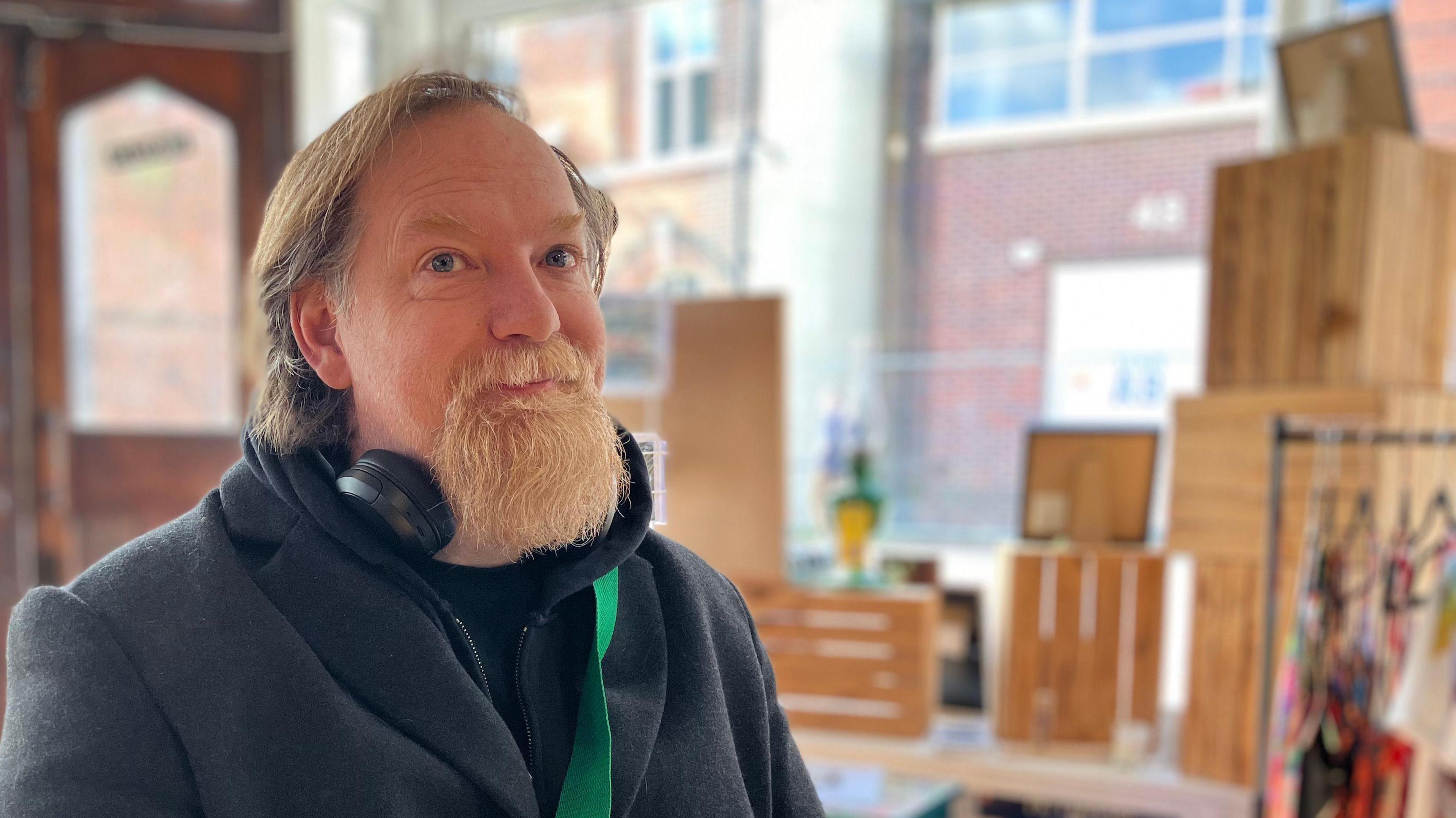 Matthew Applegate, with headphones round his neck, sits at a table inside a room, with art displays in the window behind him