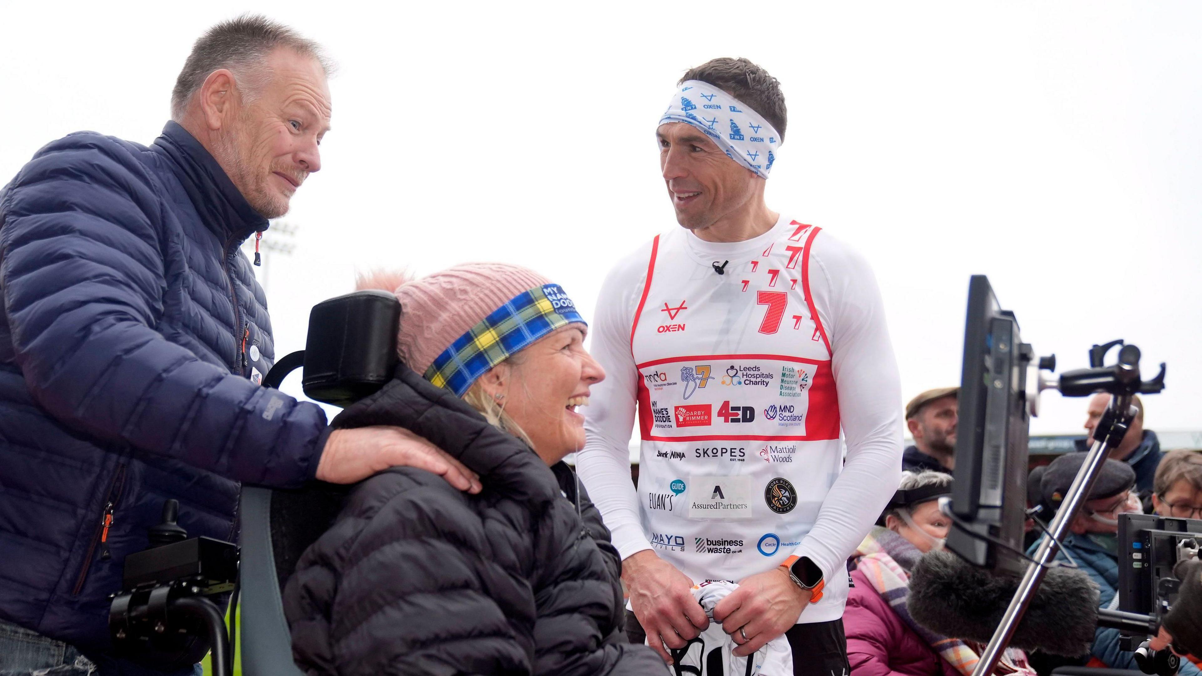 Sinfield talks to a man assisting a woman in an MND wheelchair at a running event