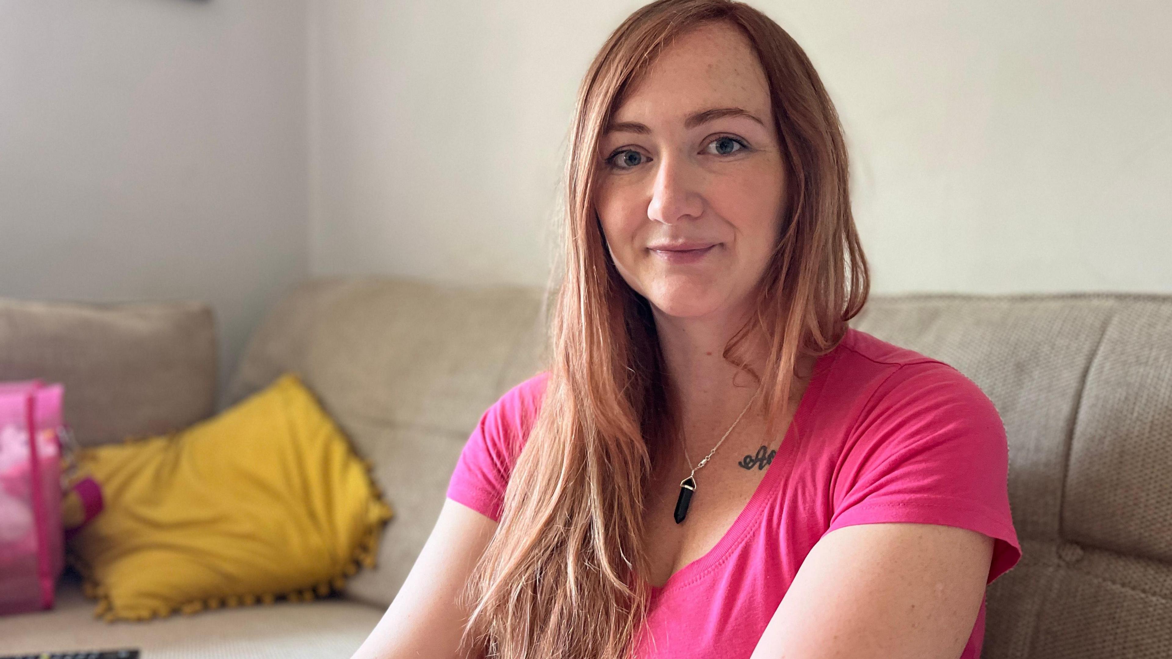 Eilish Flanagan, wearing a pink T-shirt, sits on a sofa in her living room.