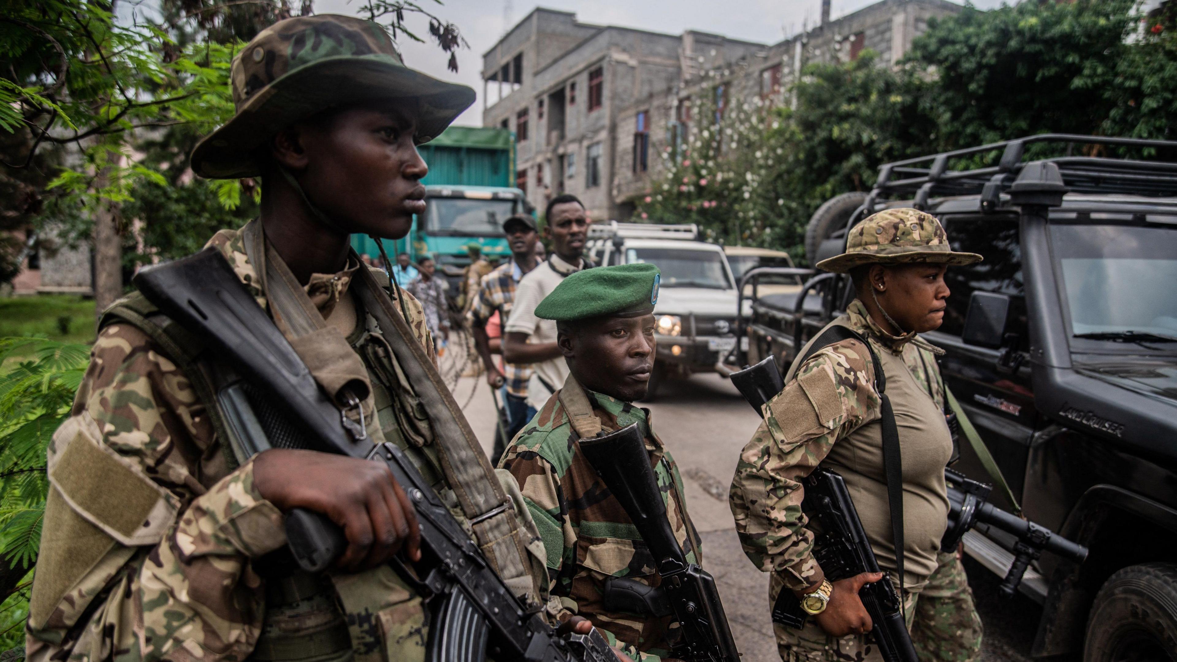 Members of the M23 movement wear camouflage fatigues and hold guns as they stand guard over a convoy of vehicles and people at the the main border crossing between DR Congo and Rwanda in Goma.