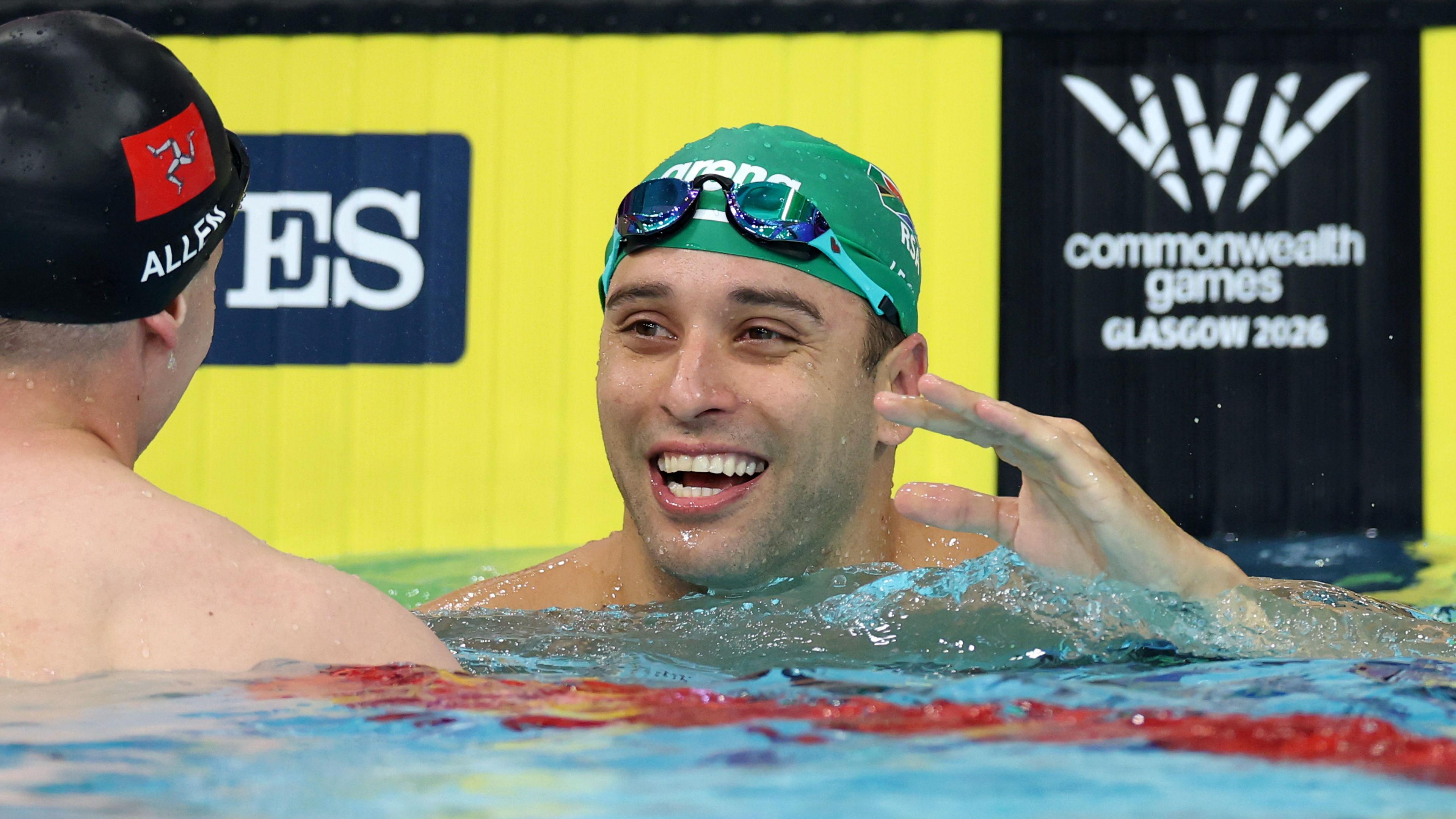 Chad le Clos smiles in a swimming pool. He is wearing goggles and a green swimming cap.