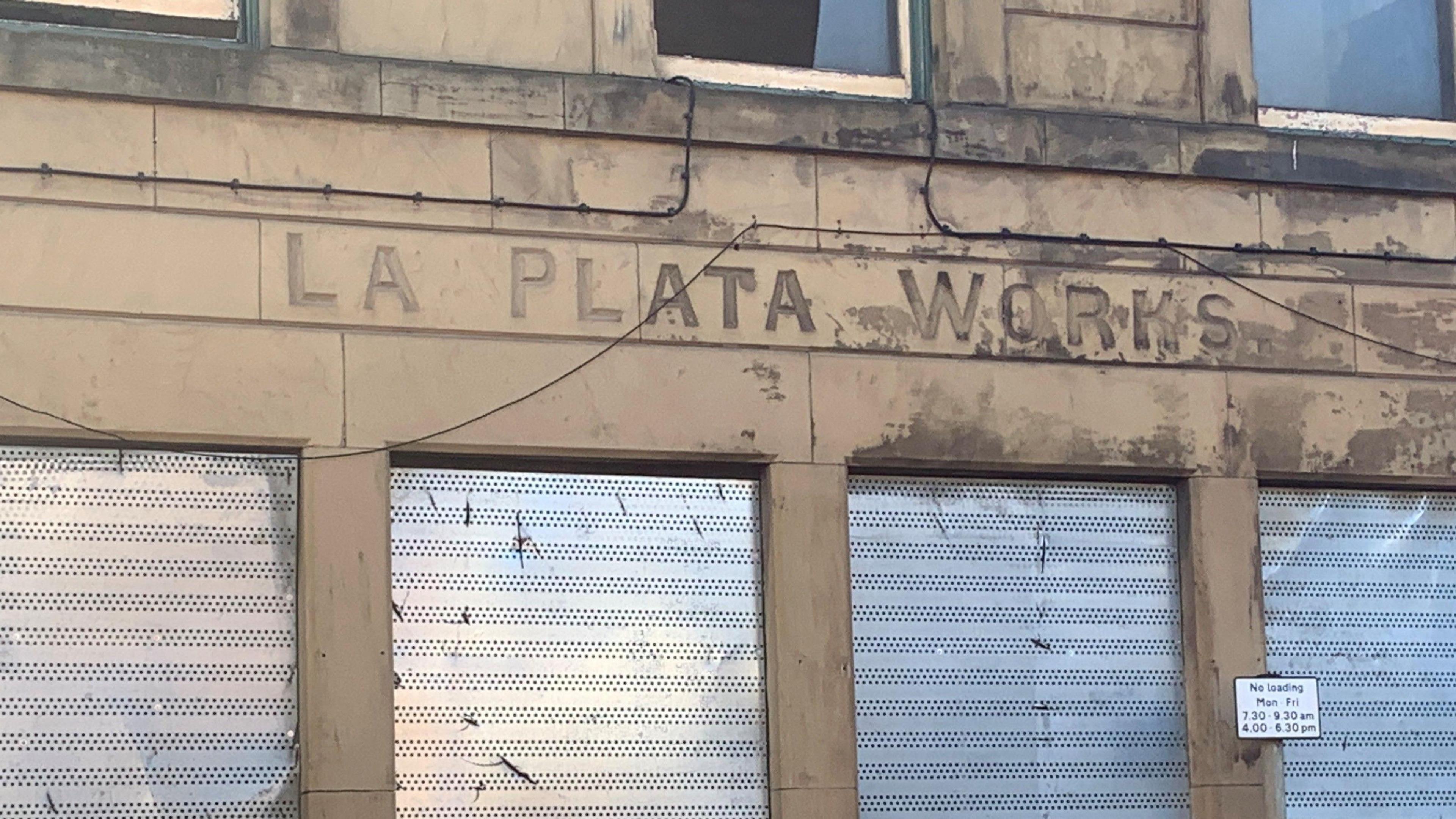 The words La Plata Works are carved into a stone building above some windows which have metal shutters covering them