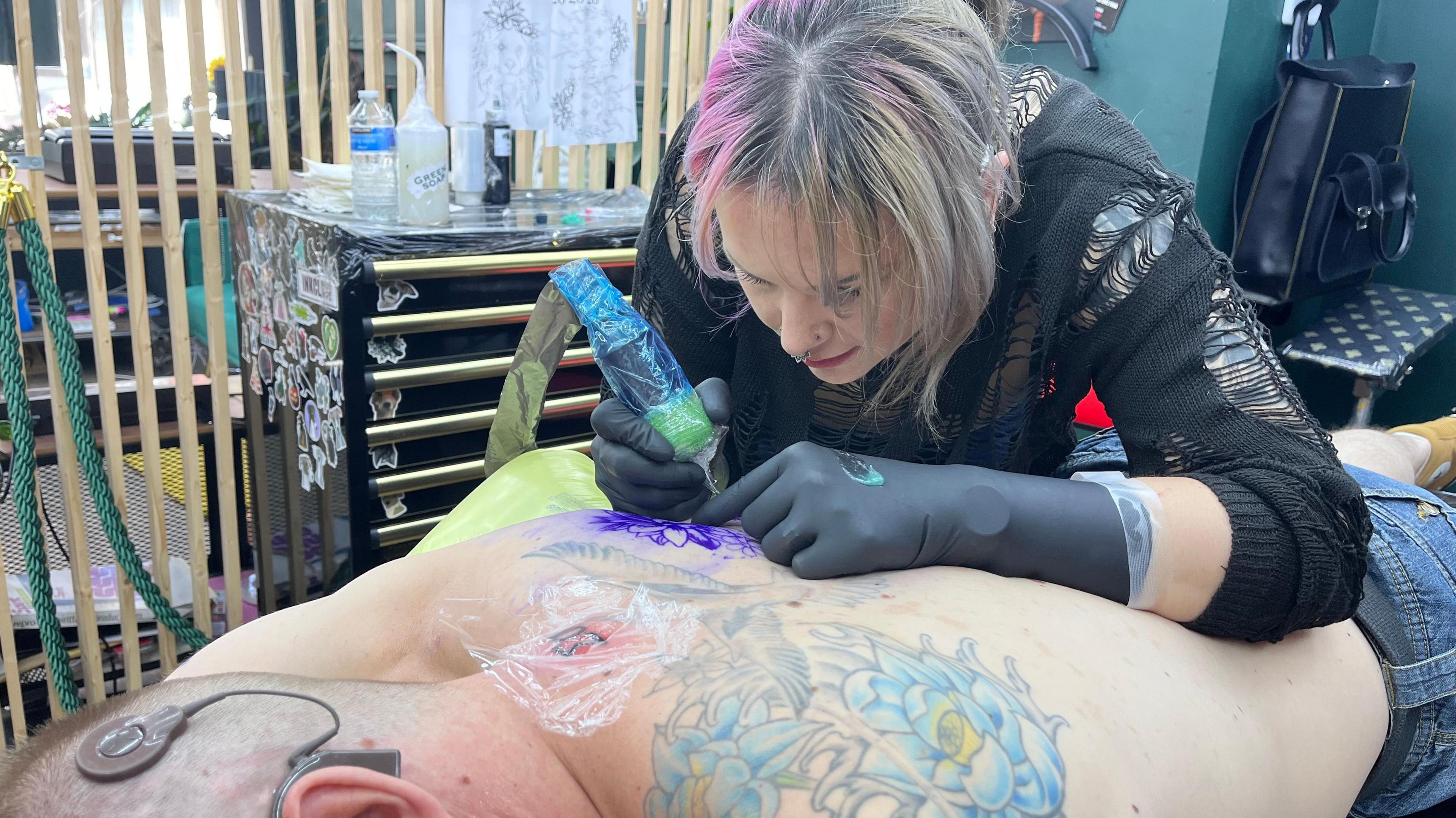 Image of Naomi Dalby tattooing the back of deaf client, Paul Gardner.