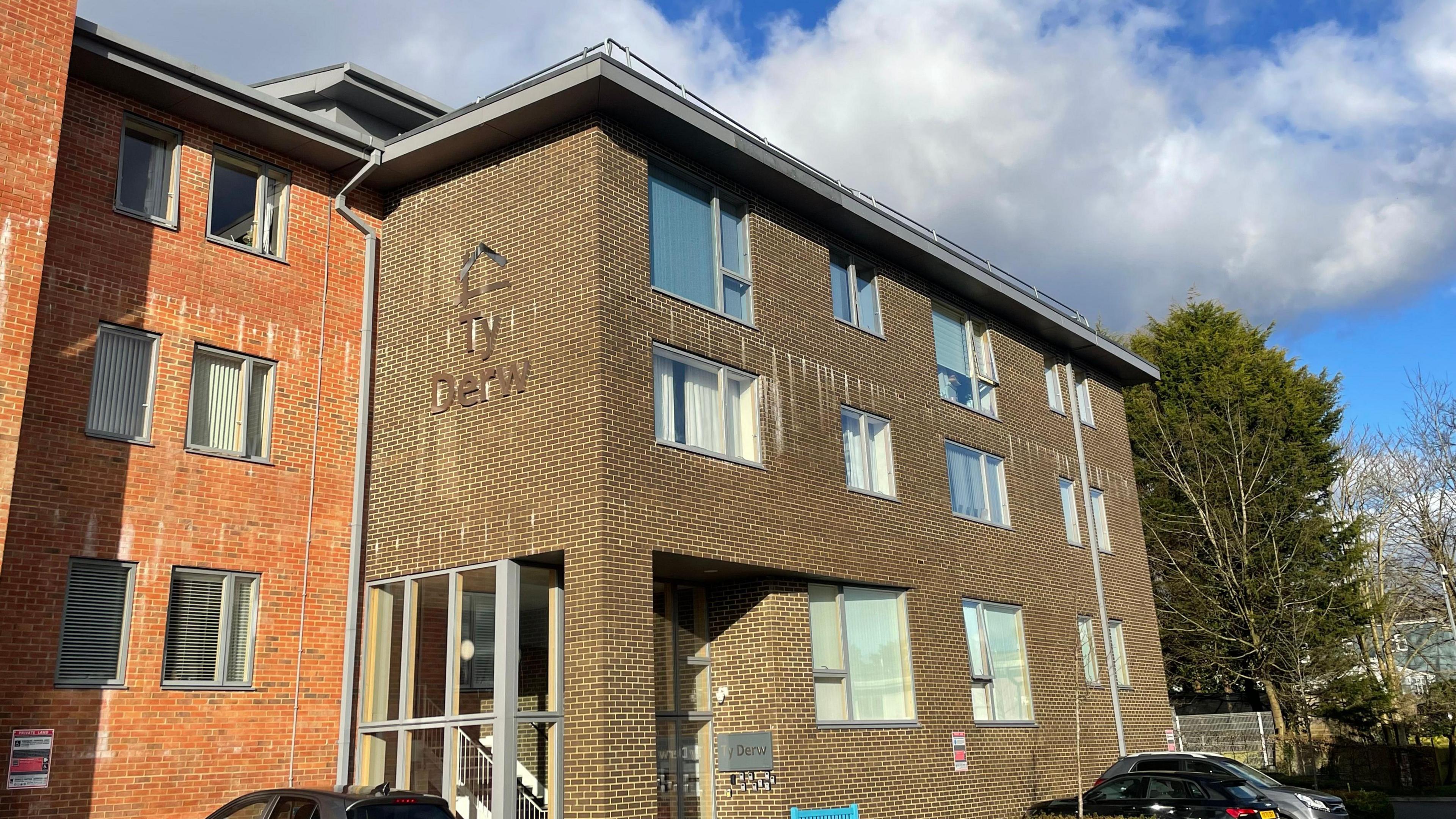 An image of the housing complex Ty Derw in Swansea. The building is a brown brick building, with windows spaced out regularly across three floors.