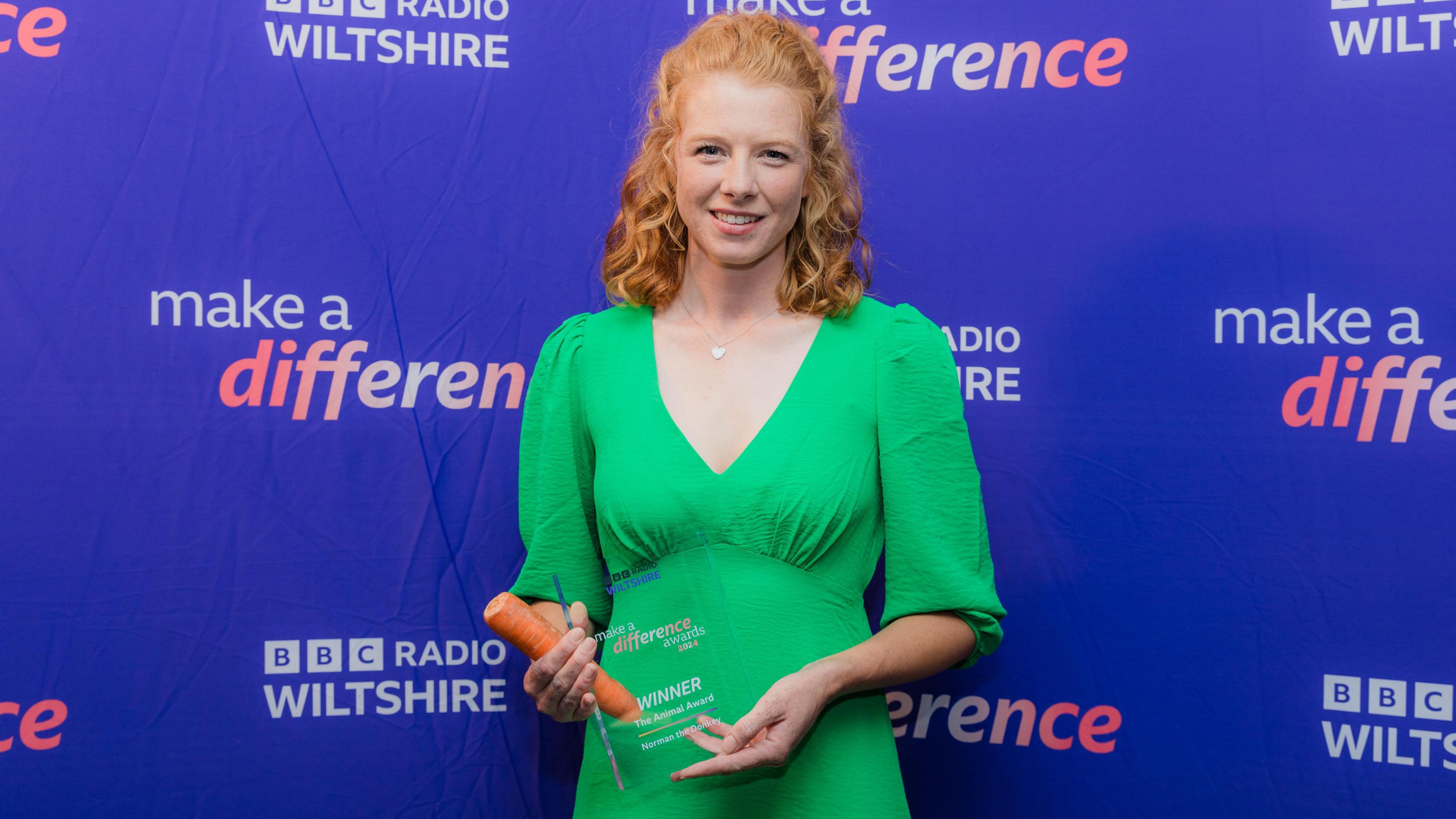 Chloe Iles wearing a green dress holds the award and a carrot - the vegetable for Norman the donkey 