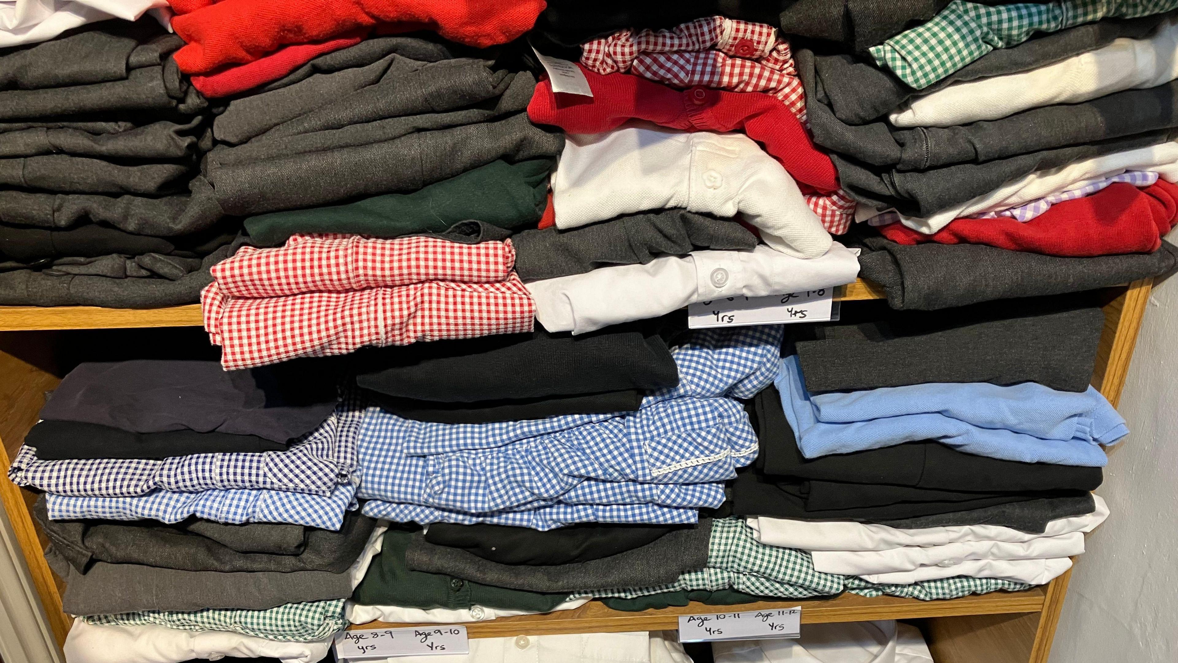 Shelves filled with school uniforms, some of which are checkered blue/red/green and white