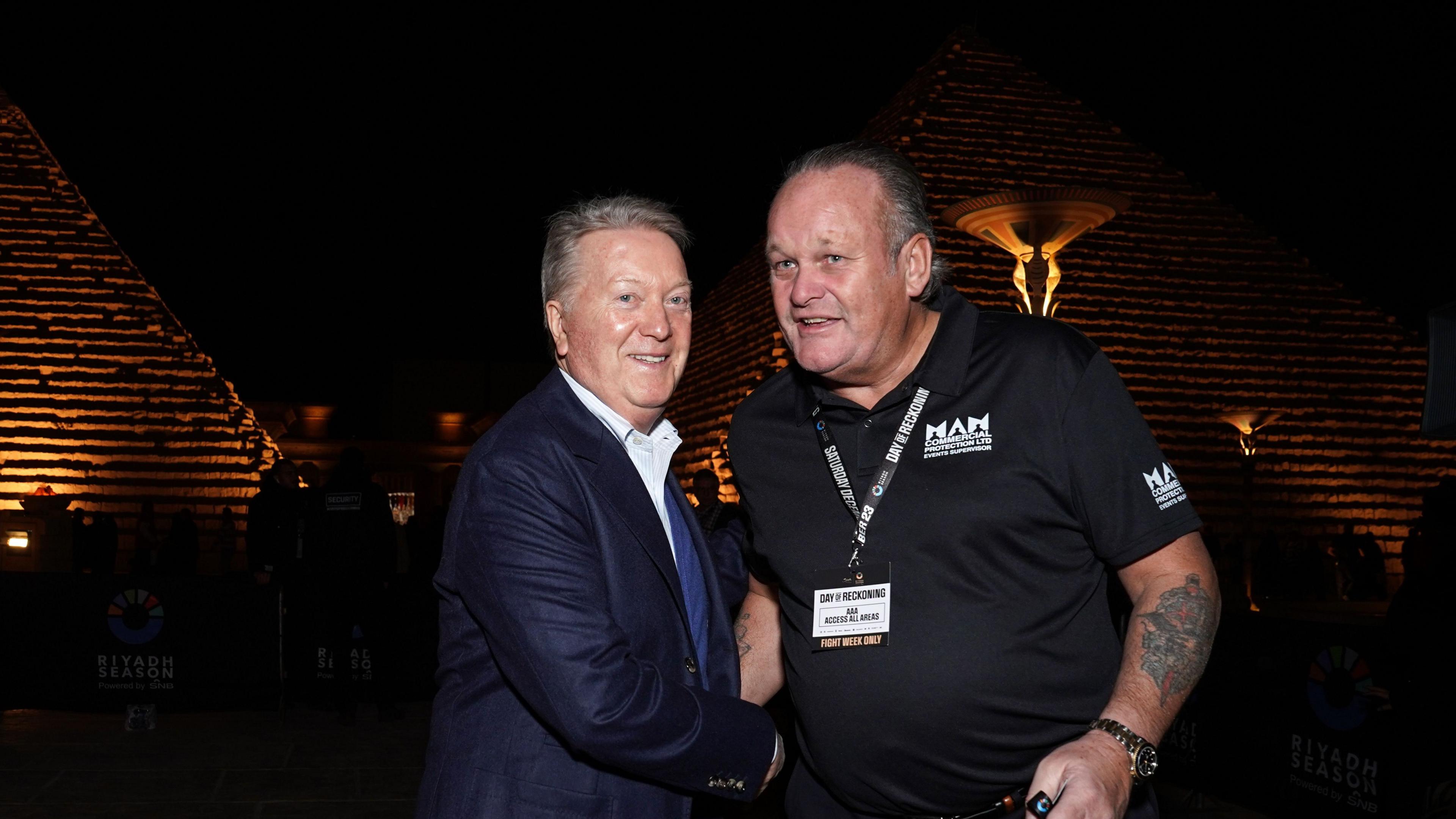 Man in a blue jacket shaking hands with a man wearing a black polo shirt