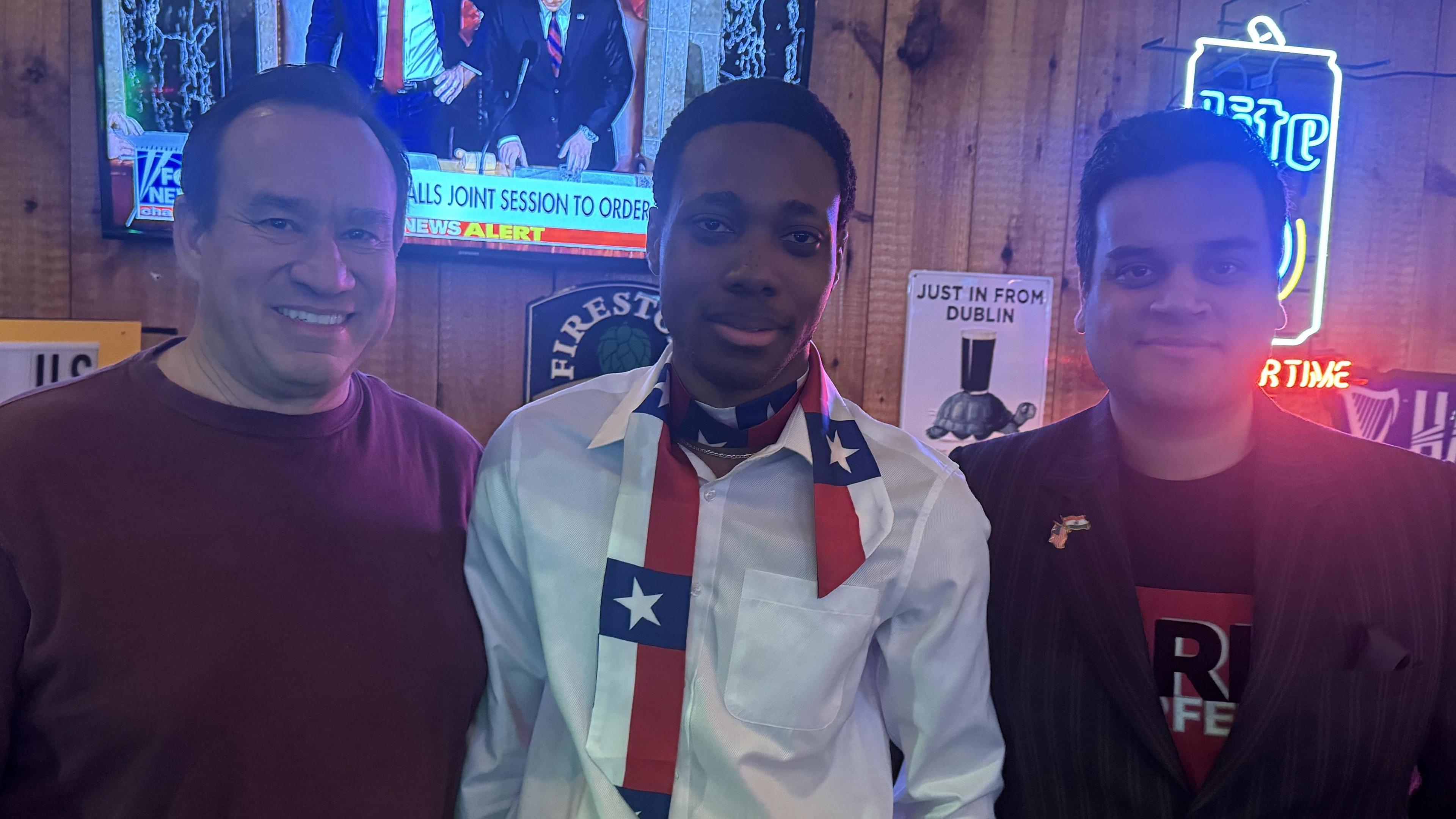 Three men wearing US-themed scarves and badges smile at the camera