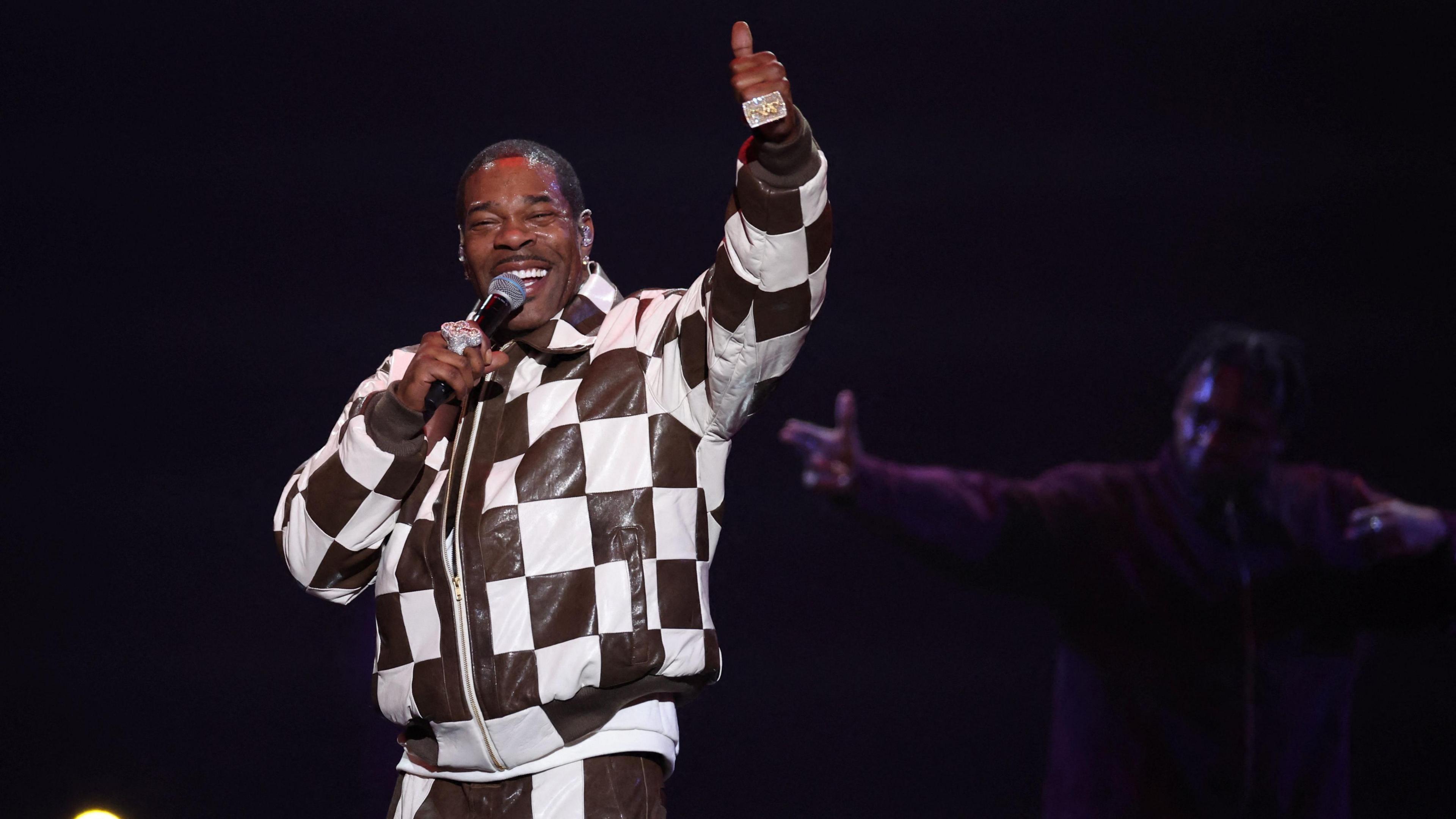 Busta Rhymes wearing a checked jacket with his thumb up