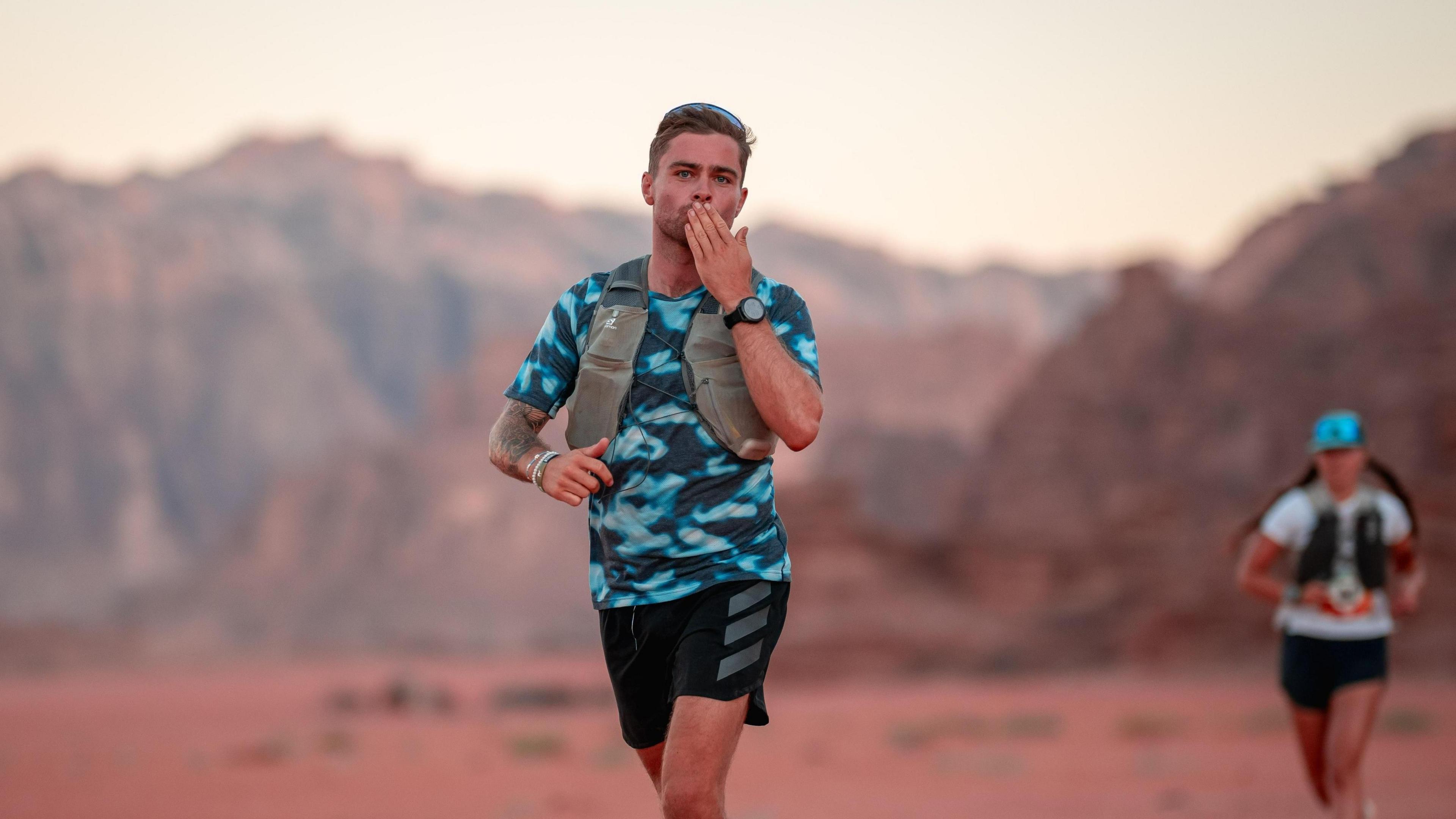 Sam King blowing a kiss to the camera while running in a desert.