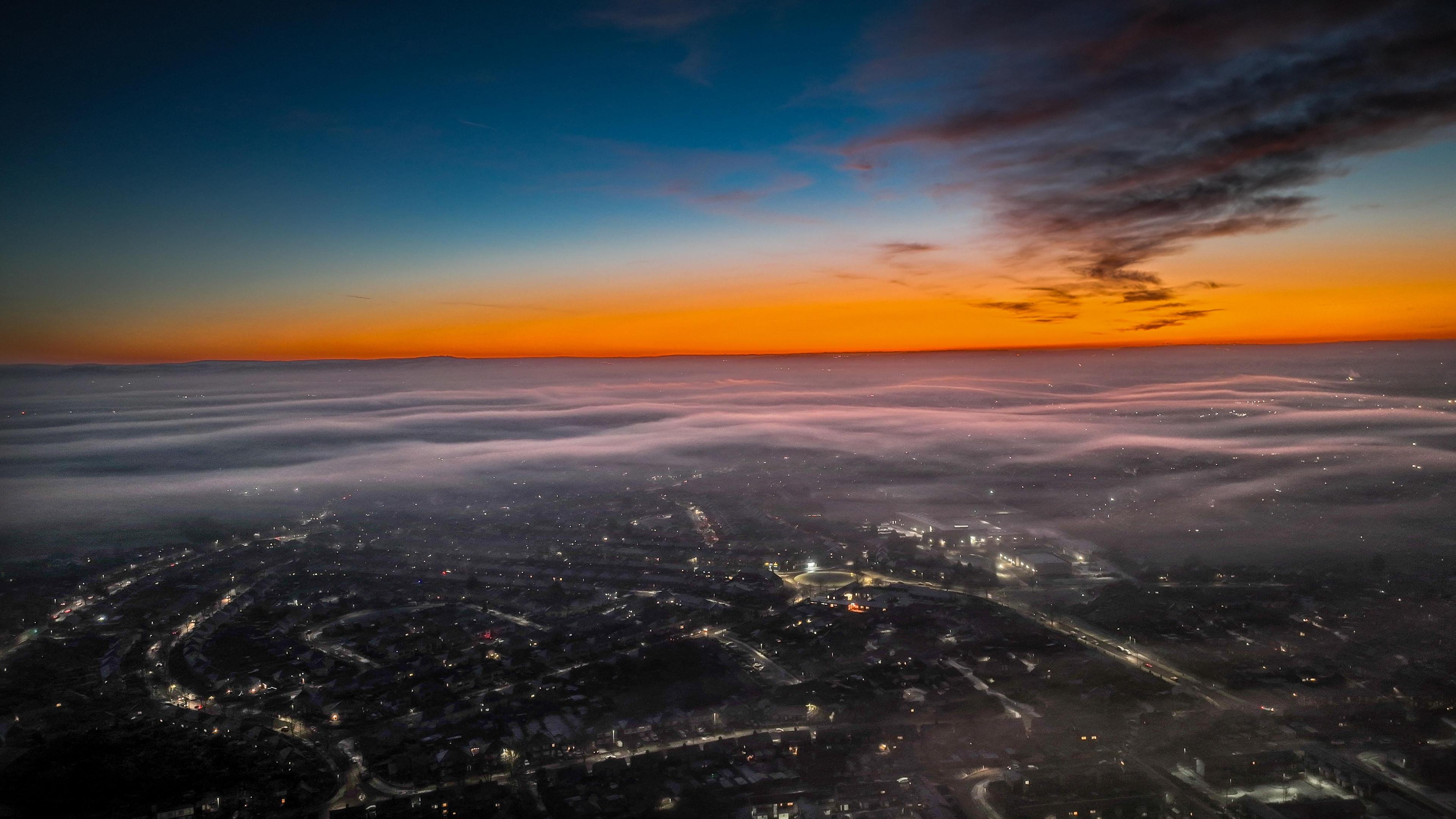 Aerial view of Church Coppenhall, near Nantwich. A low blanket of thin cloud or mist covers the area at sunset, with lights from buildings and streetlights in the distance below