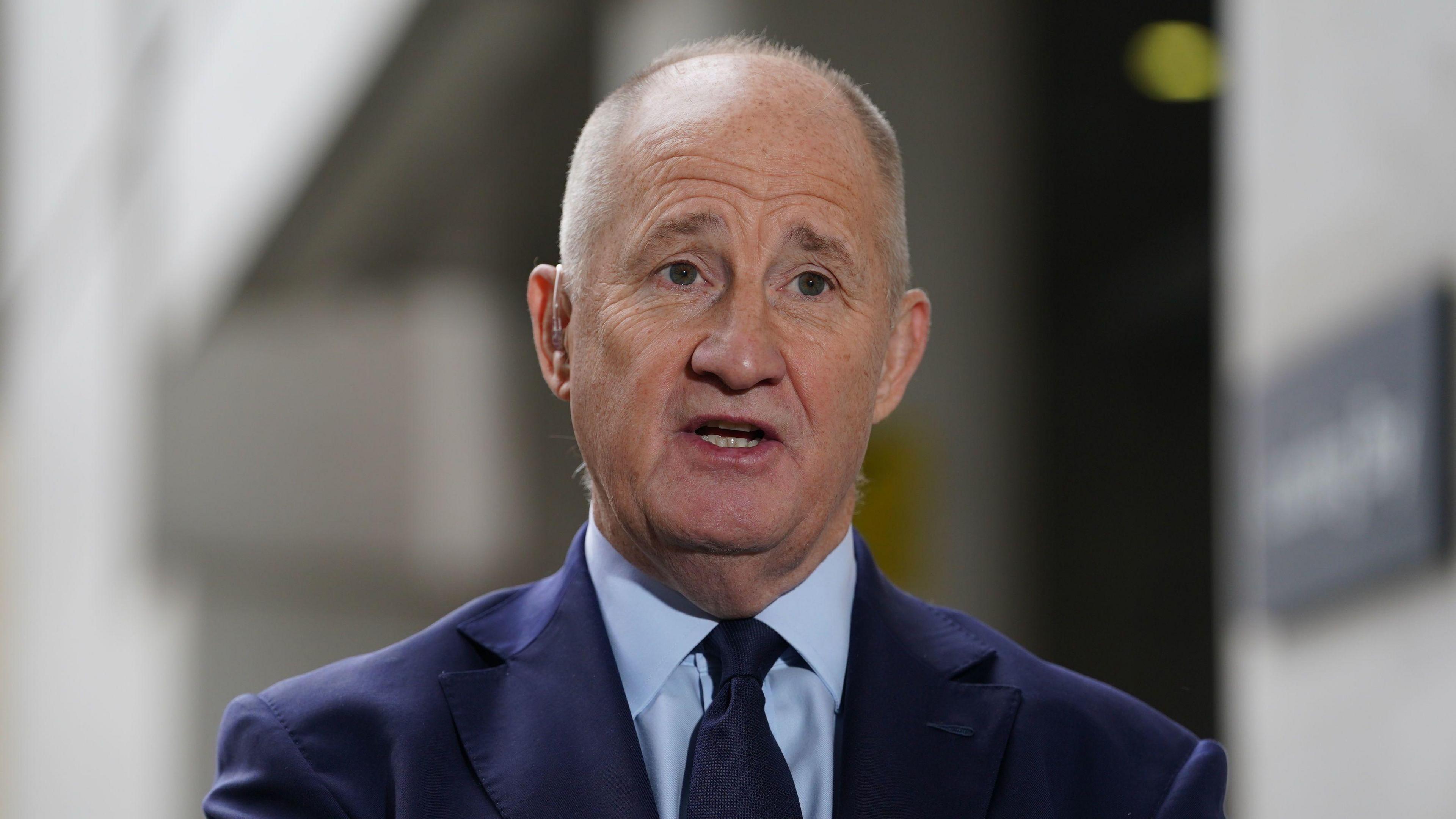 Kevin Hollinrake, who has short grey hair and wears a navy suit with a blue shirt and black tie, speaks to reporters outside a BBC building in London