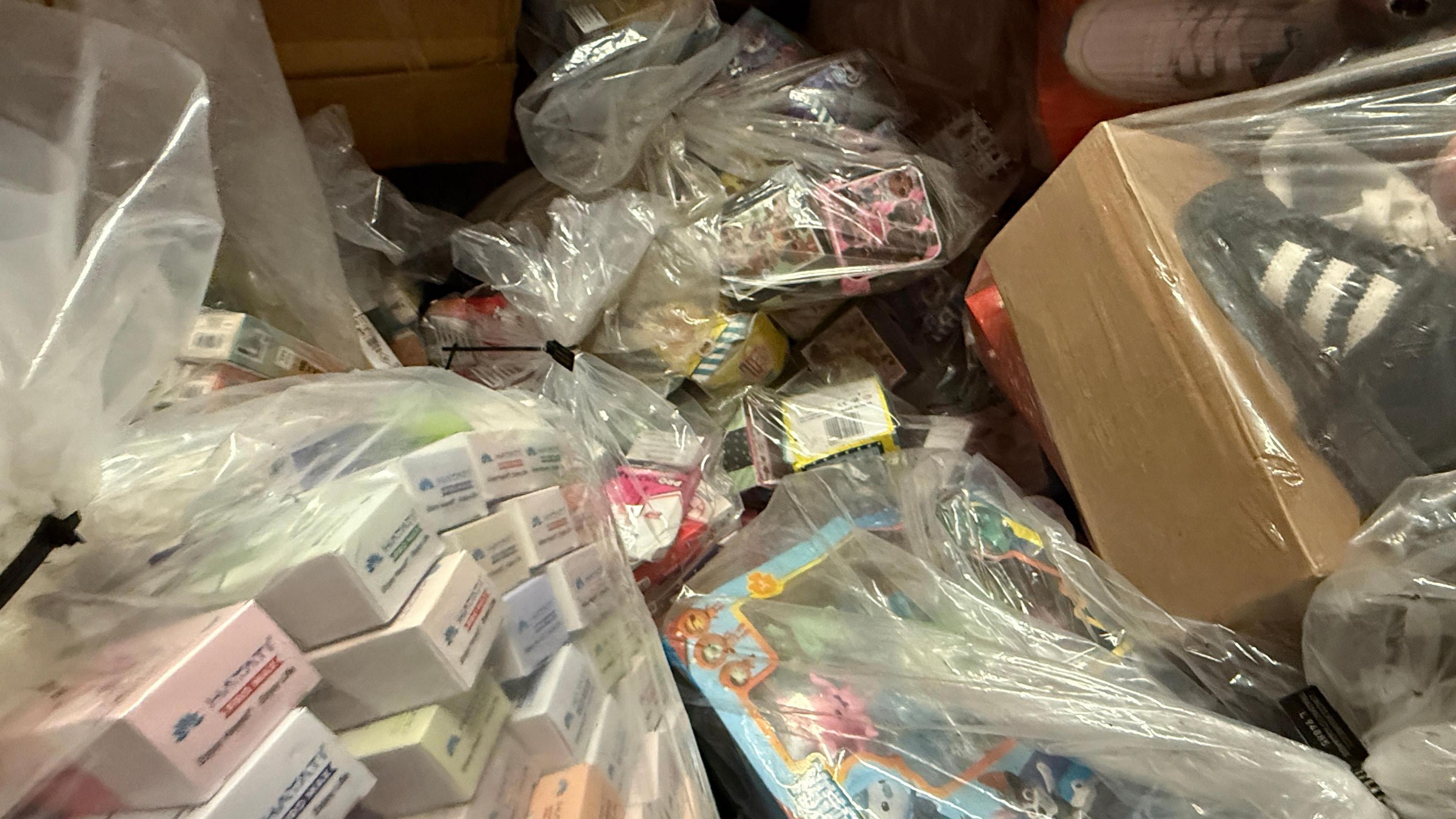 Bags of fake counterfeit items from illegal cigarettes to children's toys. A selection of shoes can also be seen in the right hand corner.