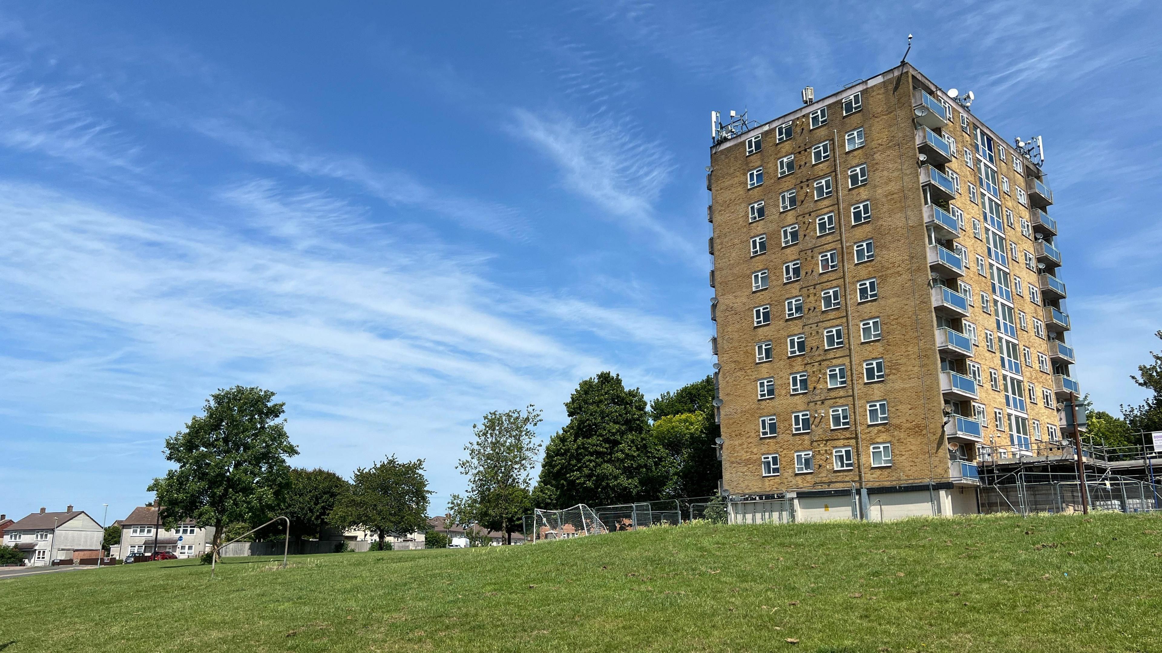 One of Penhill's tower blocks of council flats set among a playing field and blue skies, with the lower levels surrounded by scaffolding.