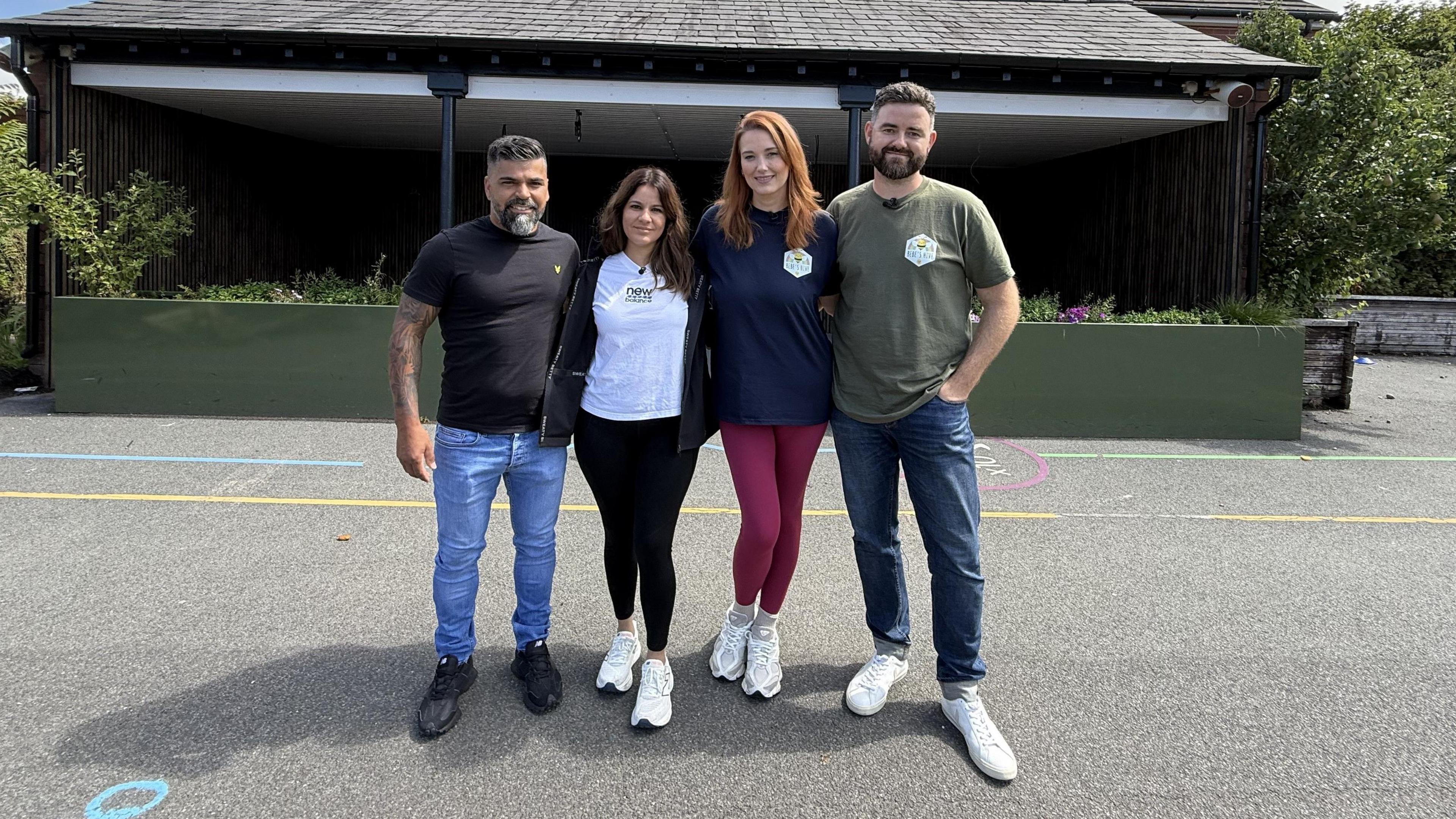 Sergio and Alex Aguiar and Lauren and Ben King are posing for a photograph in the middle of the playground at Churchtown Primary School. They are standing close together and have their arms around each other.
