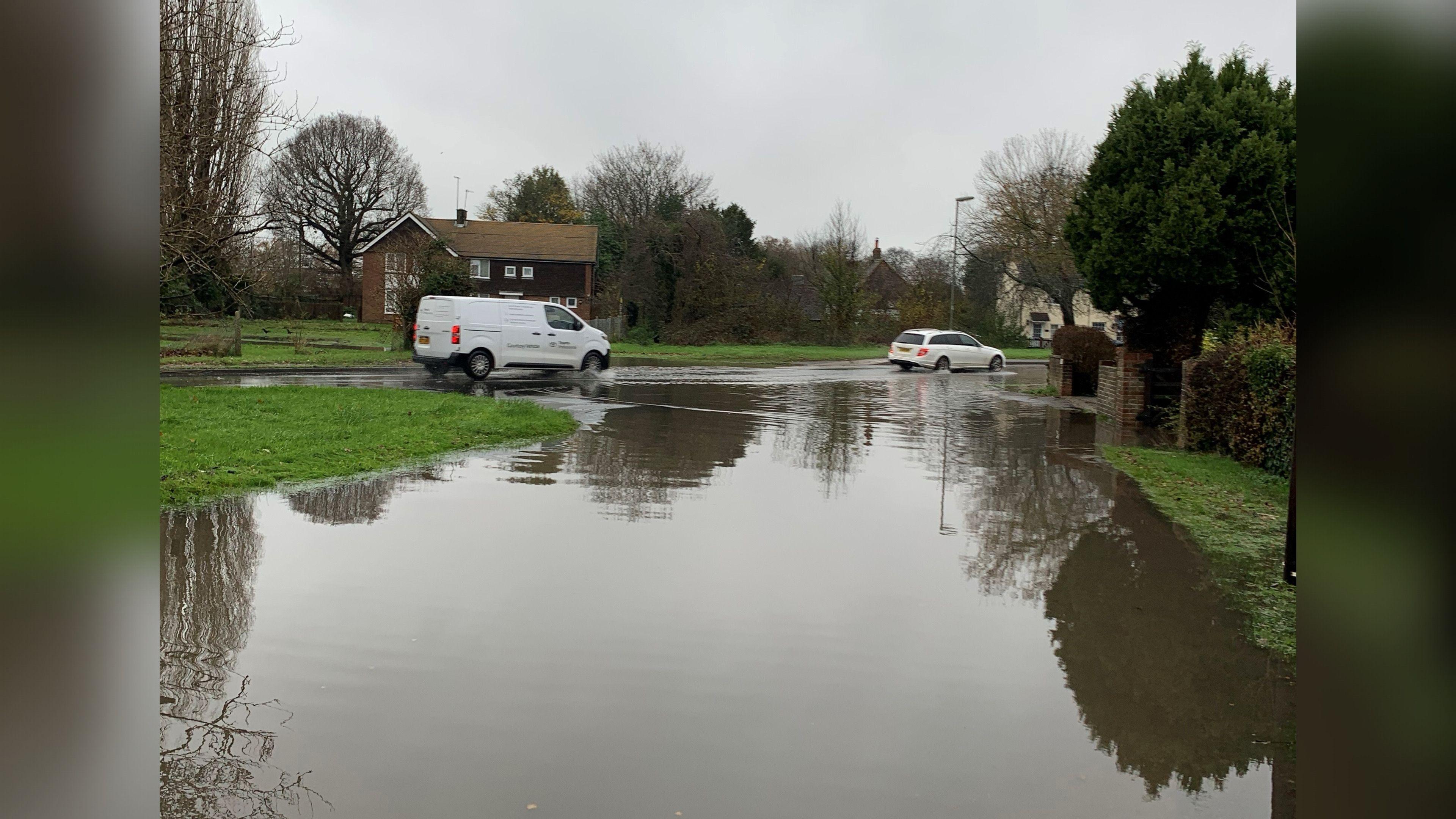 A deep puddle of sewage water with a white van and car driving through it