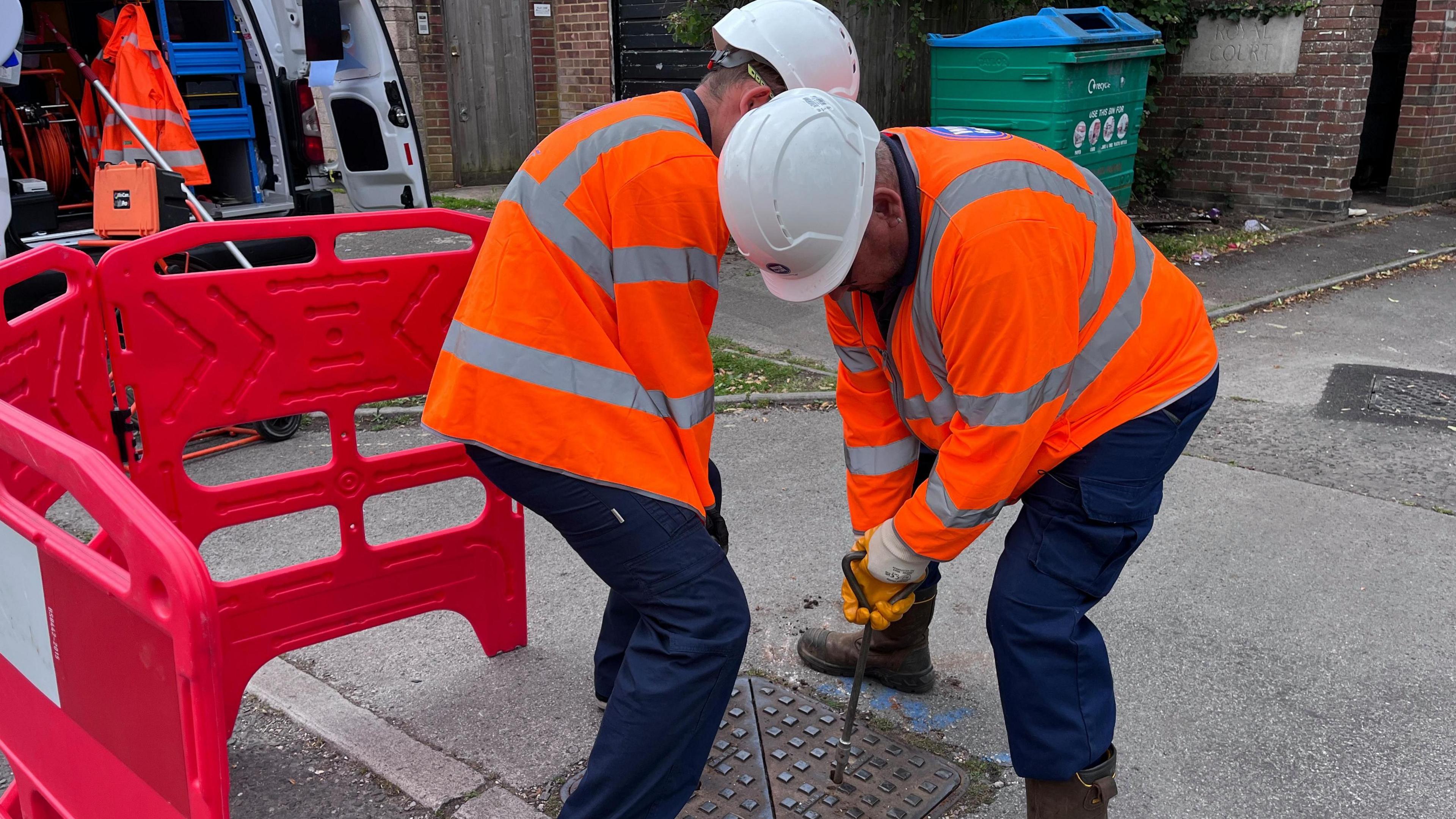 Two workmen have removed a square-shaped manhole cover.