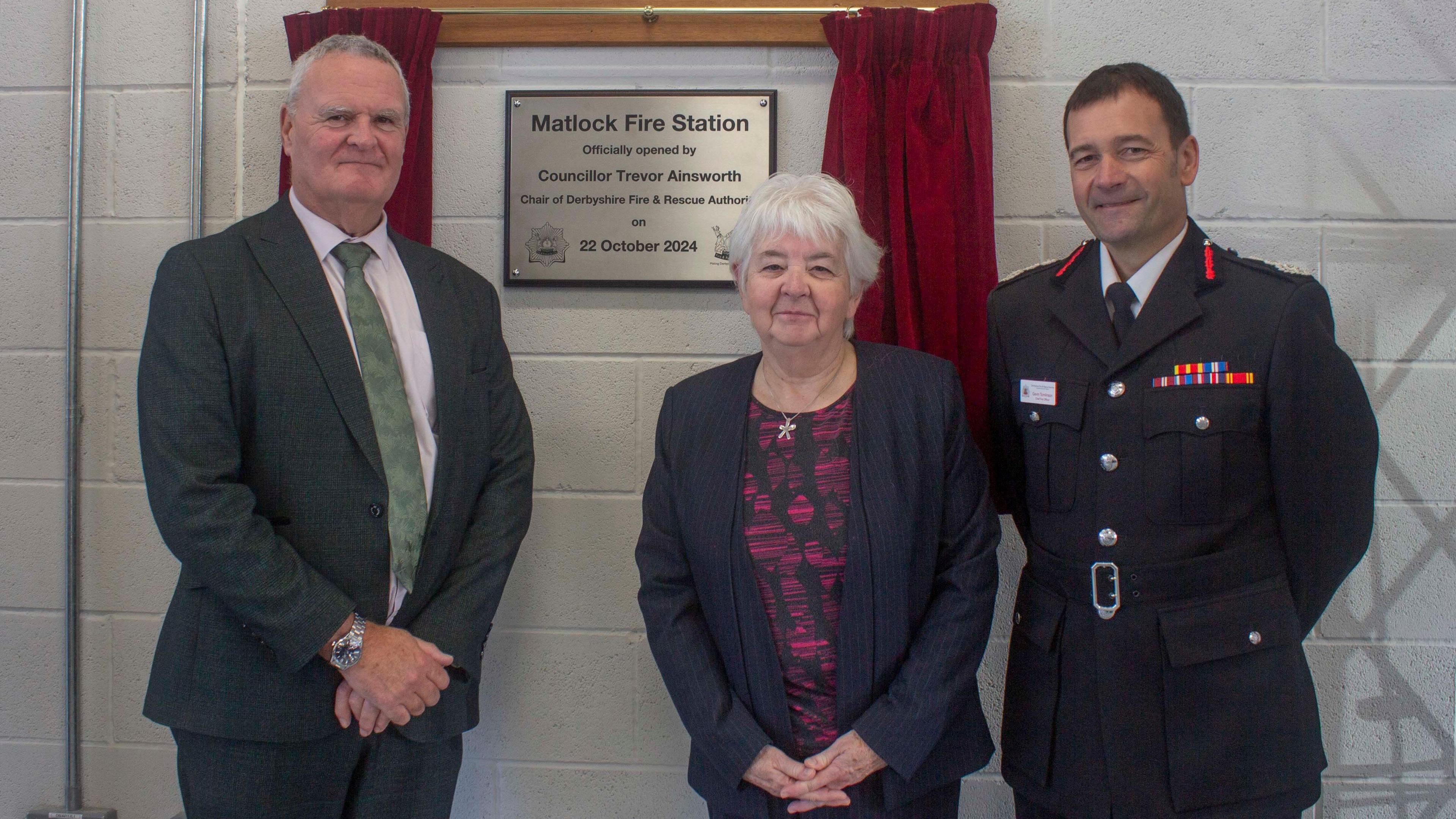 A man and a woman with grey hair stood next to a man wearing fire rescue uniform at a plaque unveiling in Matlock