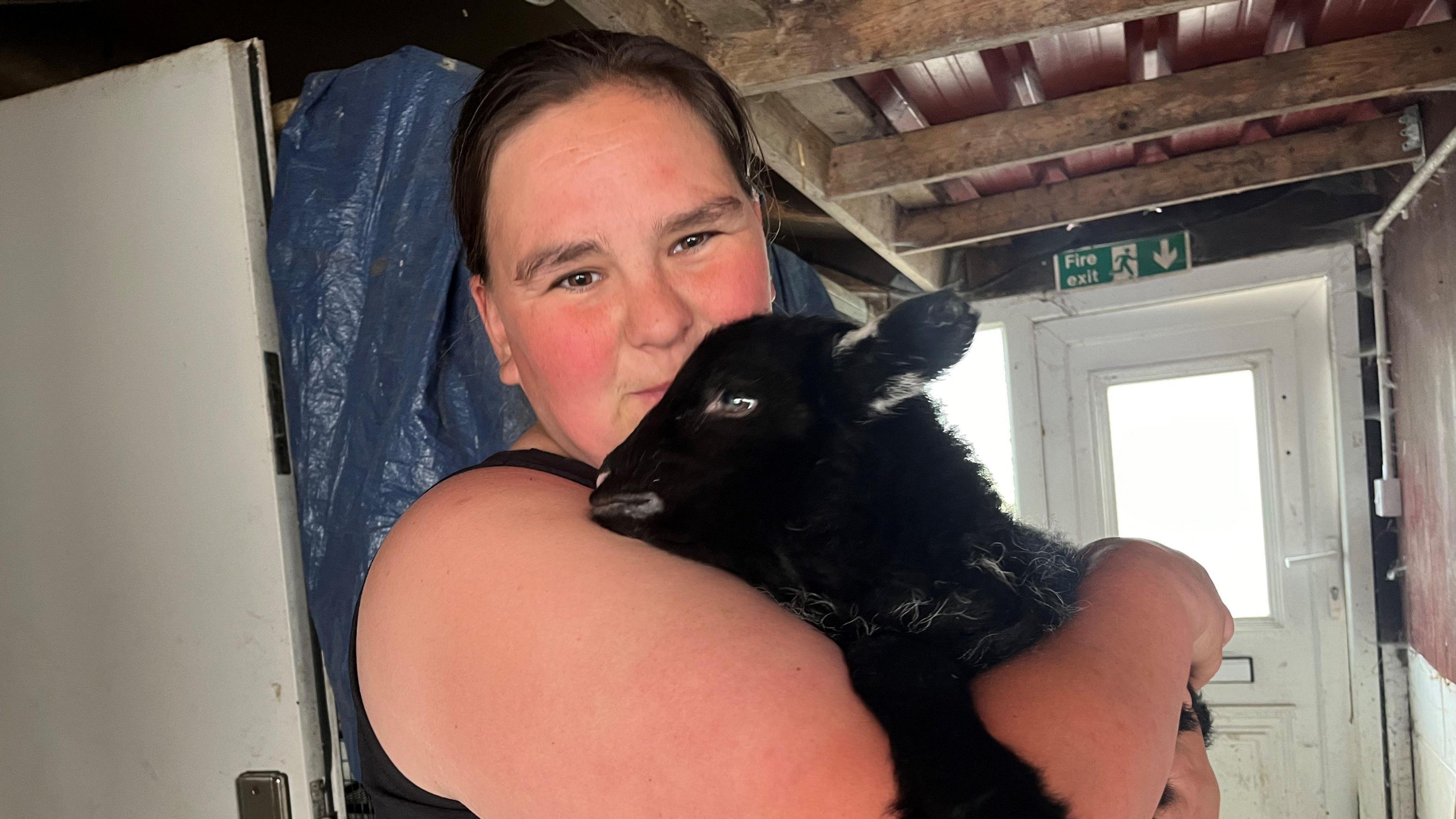 Emma Townsend with long dark hair holds a black sheep