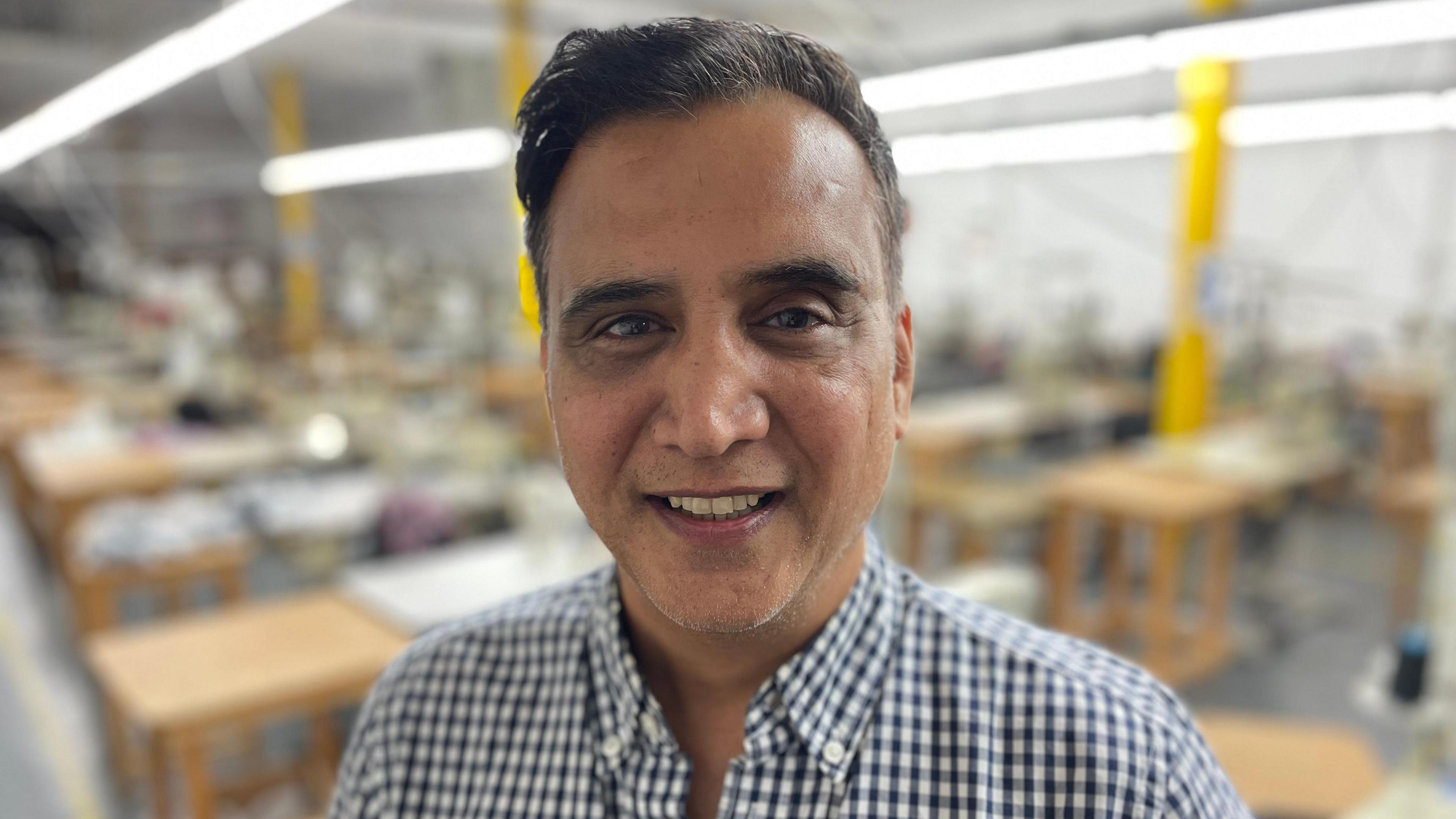 Alkesh Kapadia, pictured in a chequered shirt, smiling in a factory in Leicester