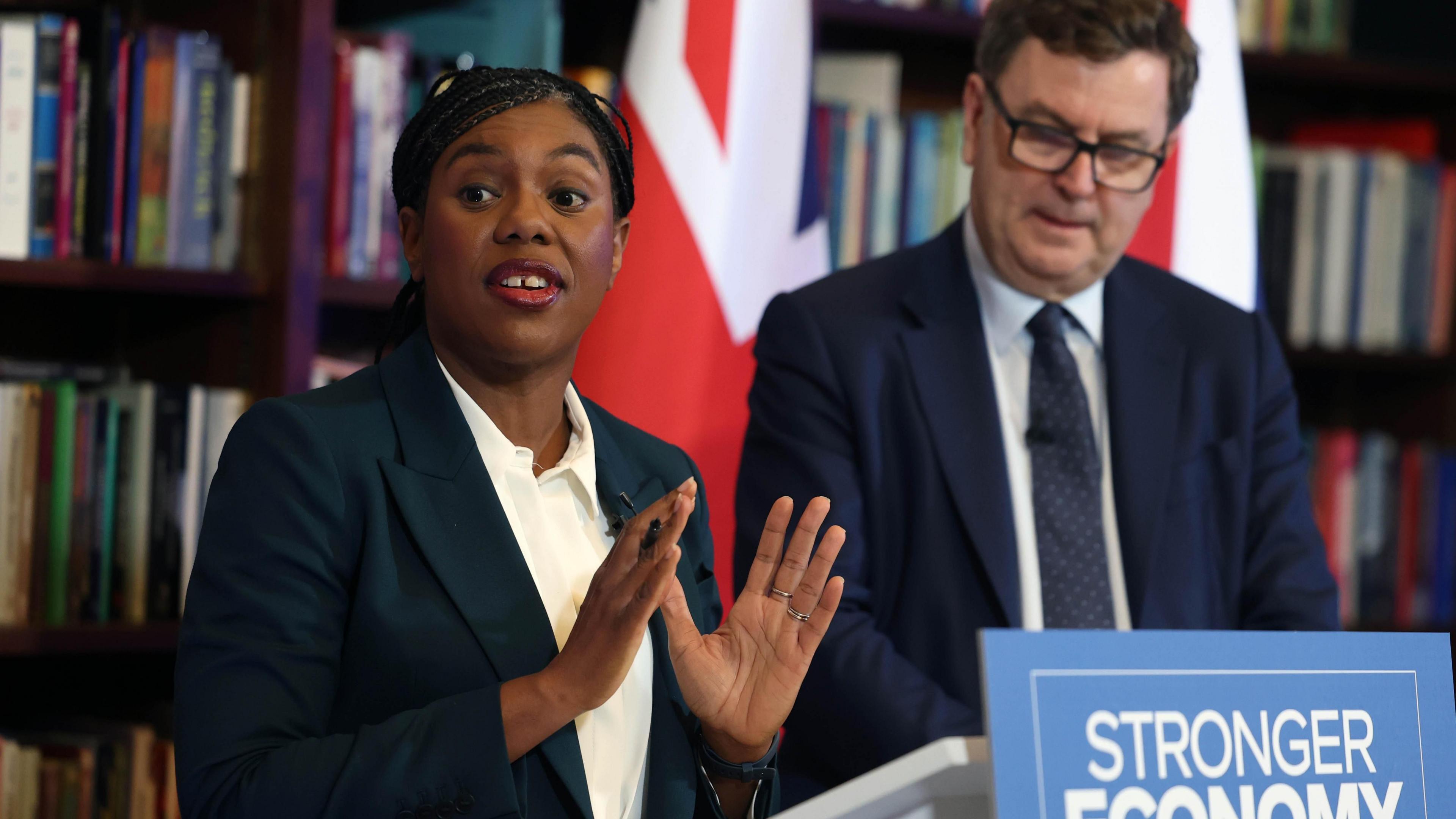 Kemi Badenoch makes a point with her hands as shadow chancellor Sir Mel Stride looks down at his notes. They are standing behind a podium with "Stronger Economy" written on it.
