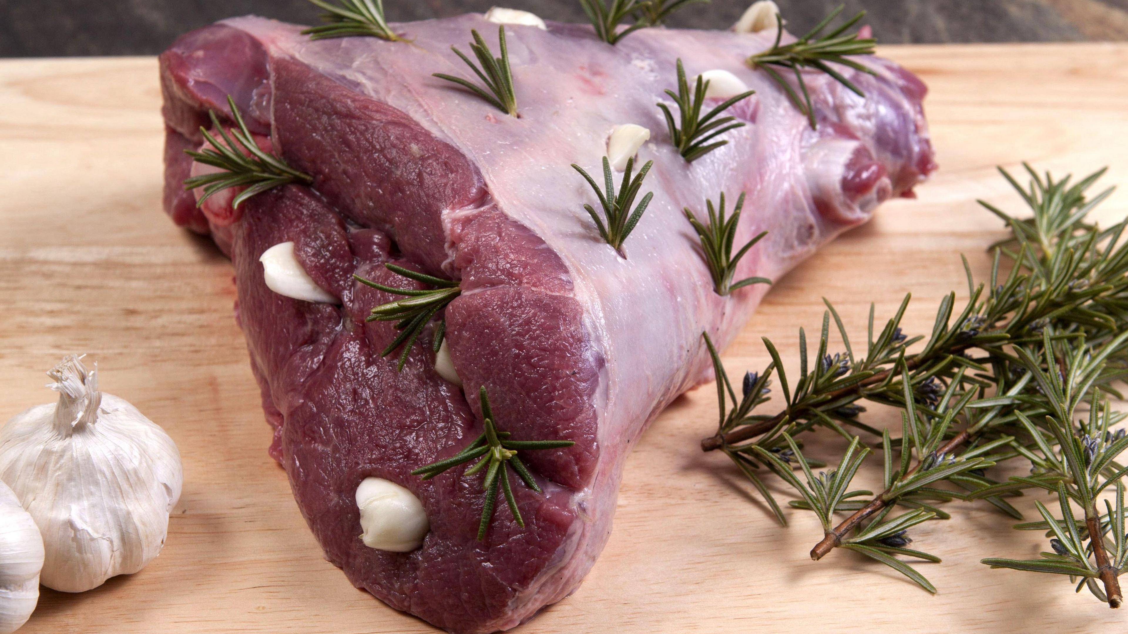 A raw leg of lamb ready for roasting. The meat has been scored and stuffed with garlic and sprigs of fresh rosemary.