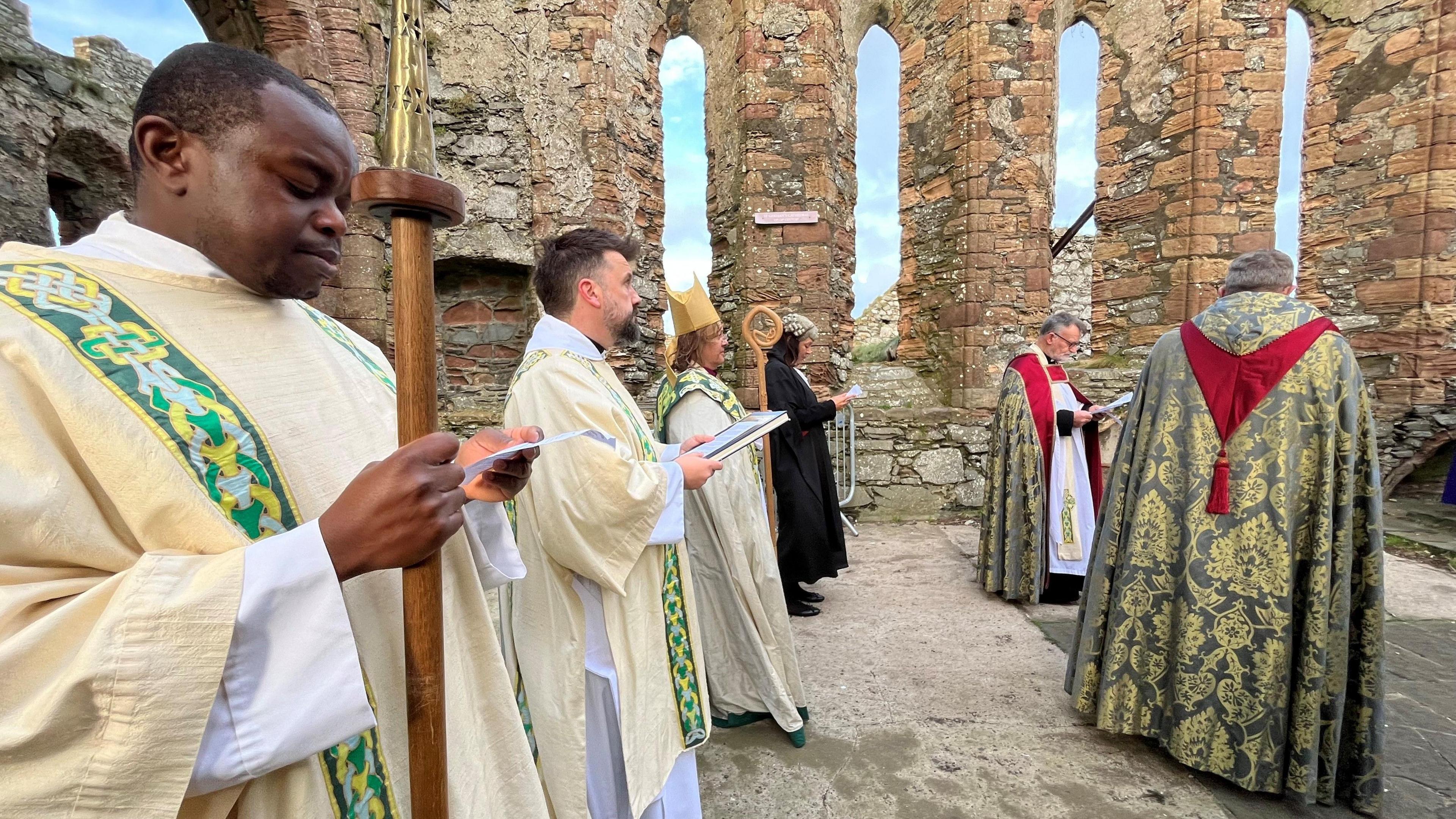 Clergy, including the Right Reverend Patrician Hillas, wearing vestments line up with in part of the ruins of St German's Cathedral, which is part of the Peel Castle site.