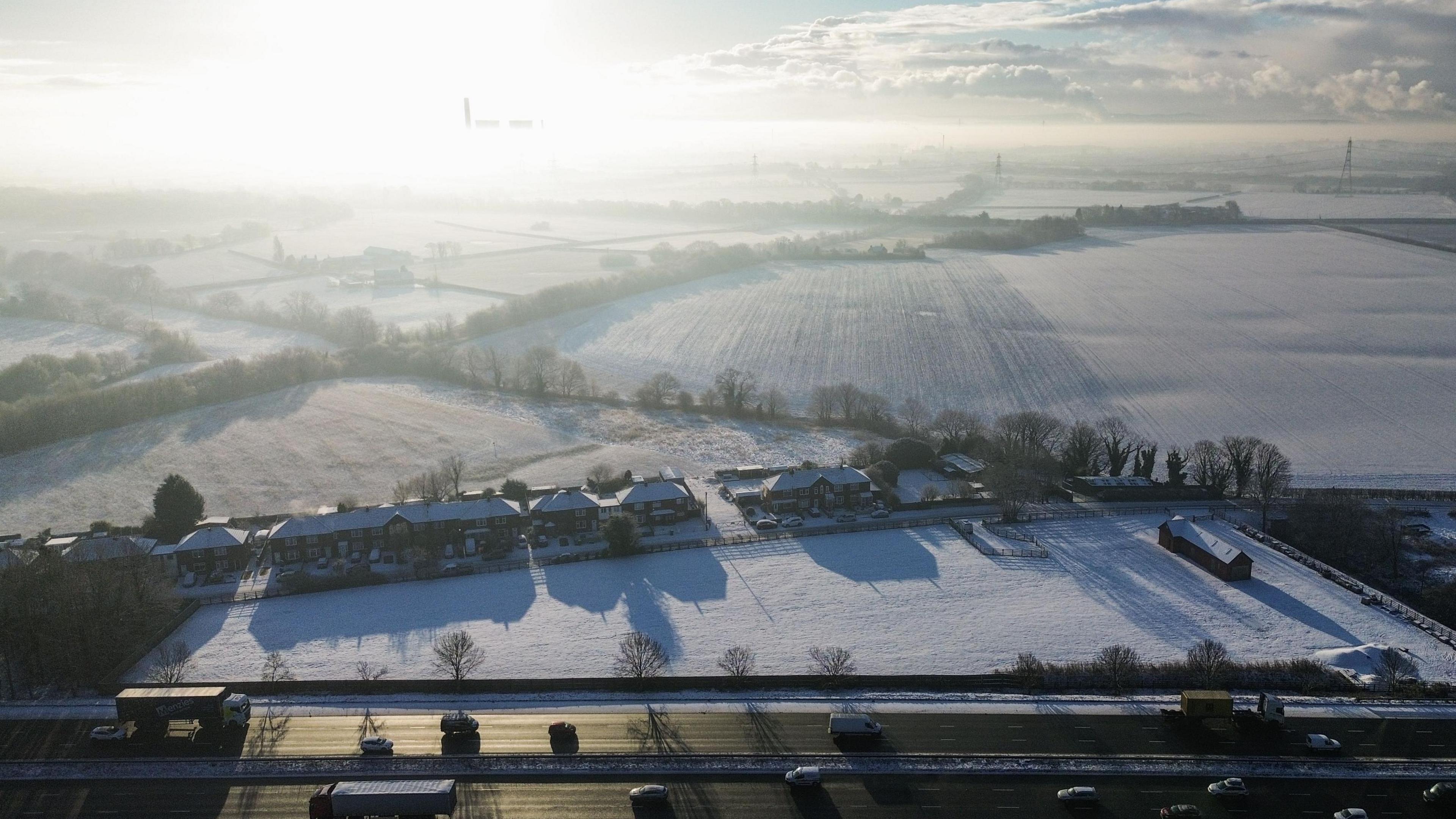 Low sun over a frozen, snowy landscape with road in foreground.